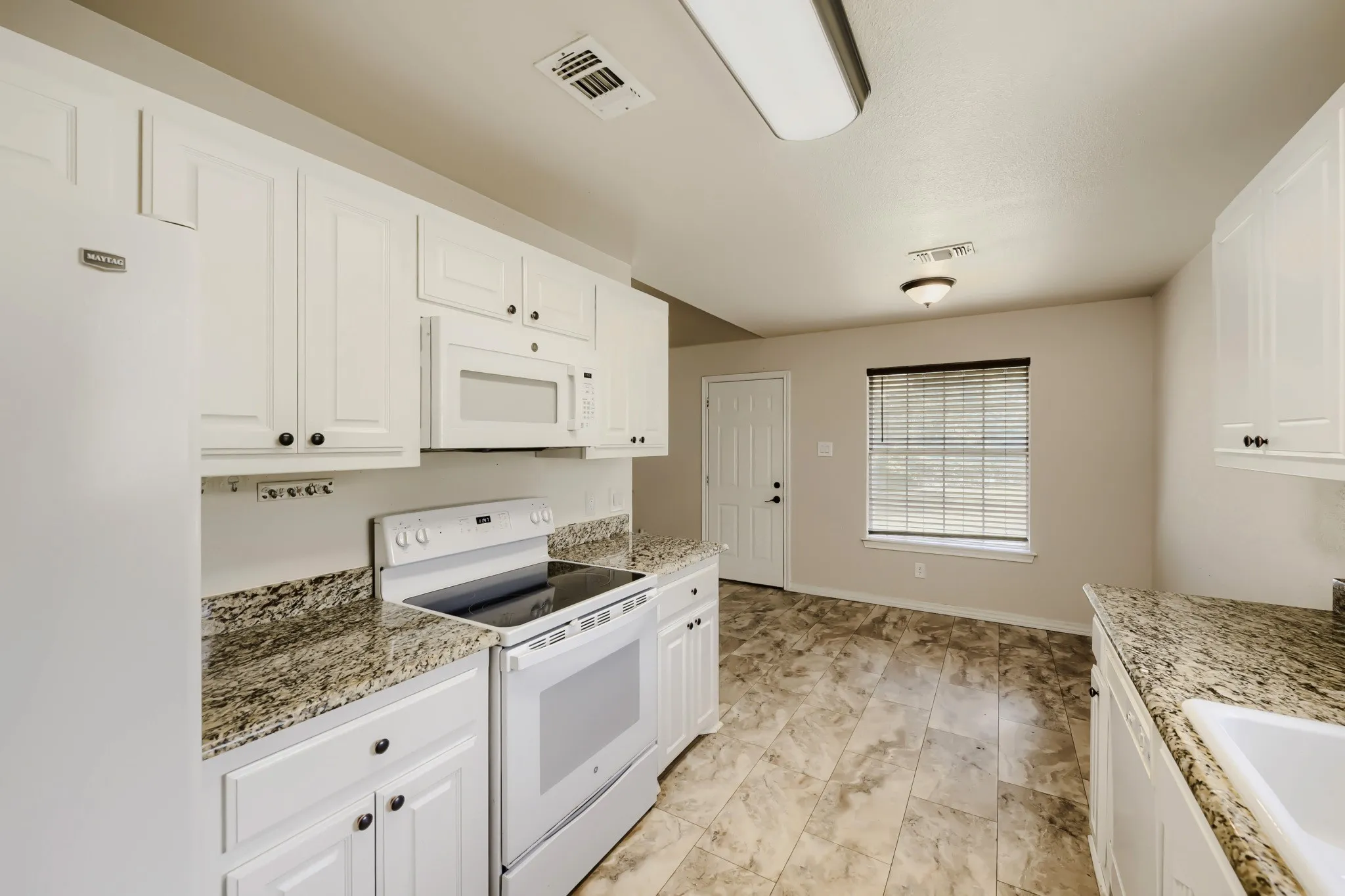 Kitchen featuring white cabinetry, granite-look countertops, and an integrated white oven and microwave