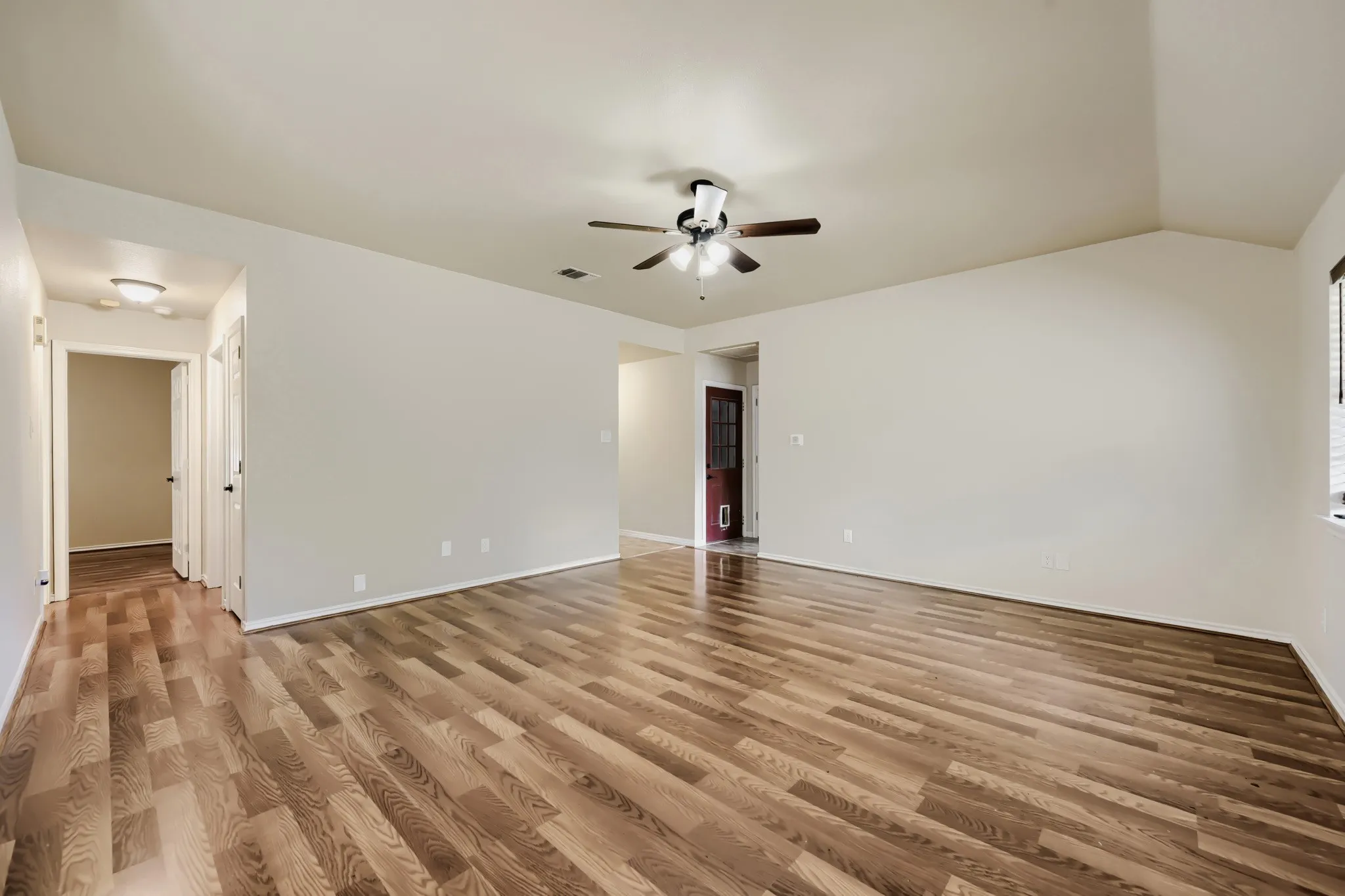 Spacious interior room featuring wood-finish flooring, vaulted ceilings, and a ceiling fan