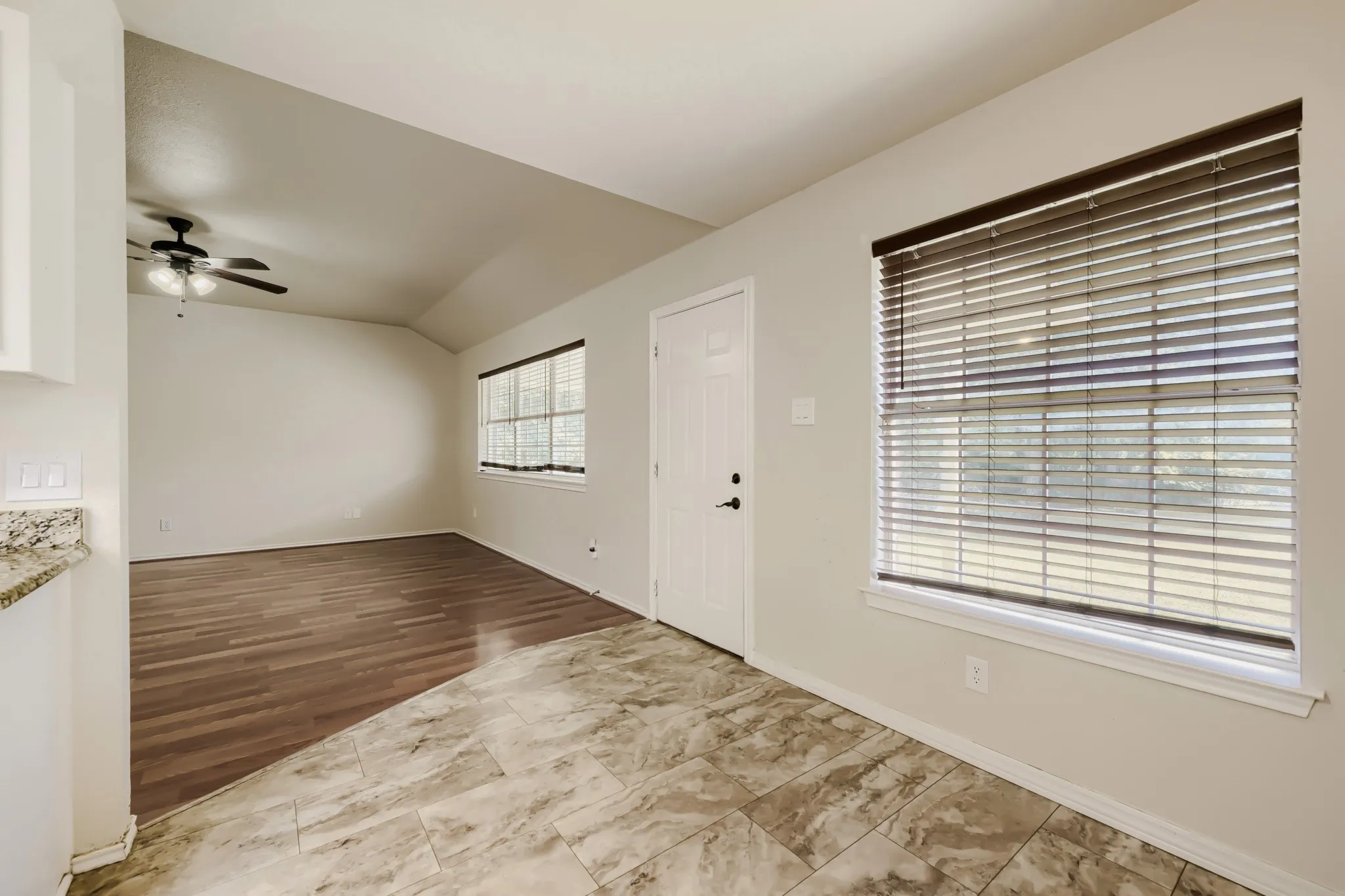 Vaulted ceiling interior featuring a ceiling fan, wood-finish flooring, and two windows with blinds