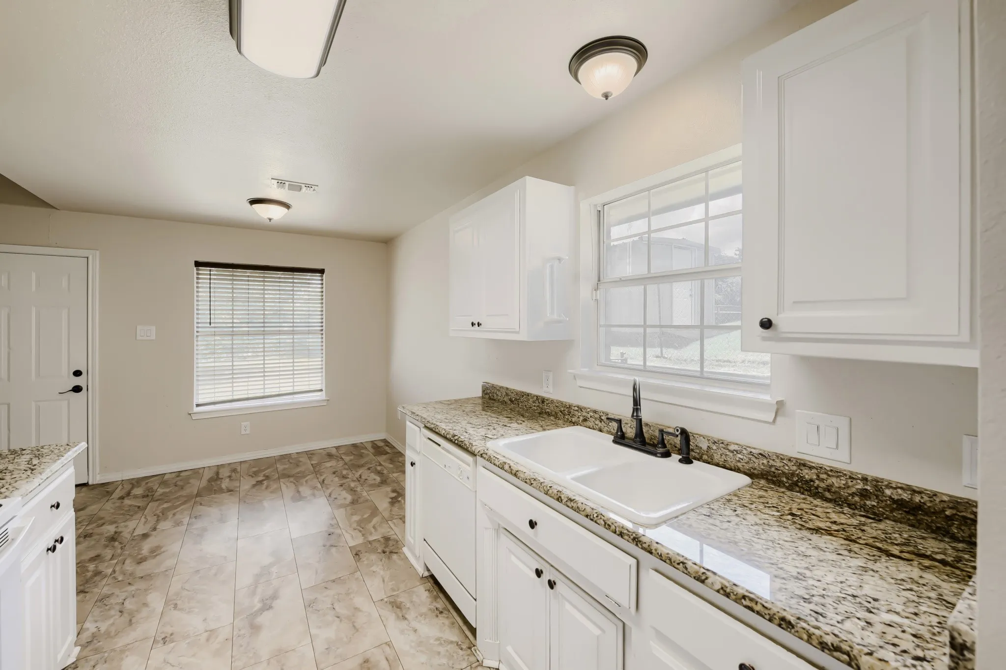 Kitchen featuring white cabinetry, stone-finish countertops, a double basin sink with a dark-finish faucet, and tile-finish flooring