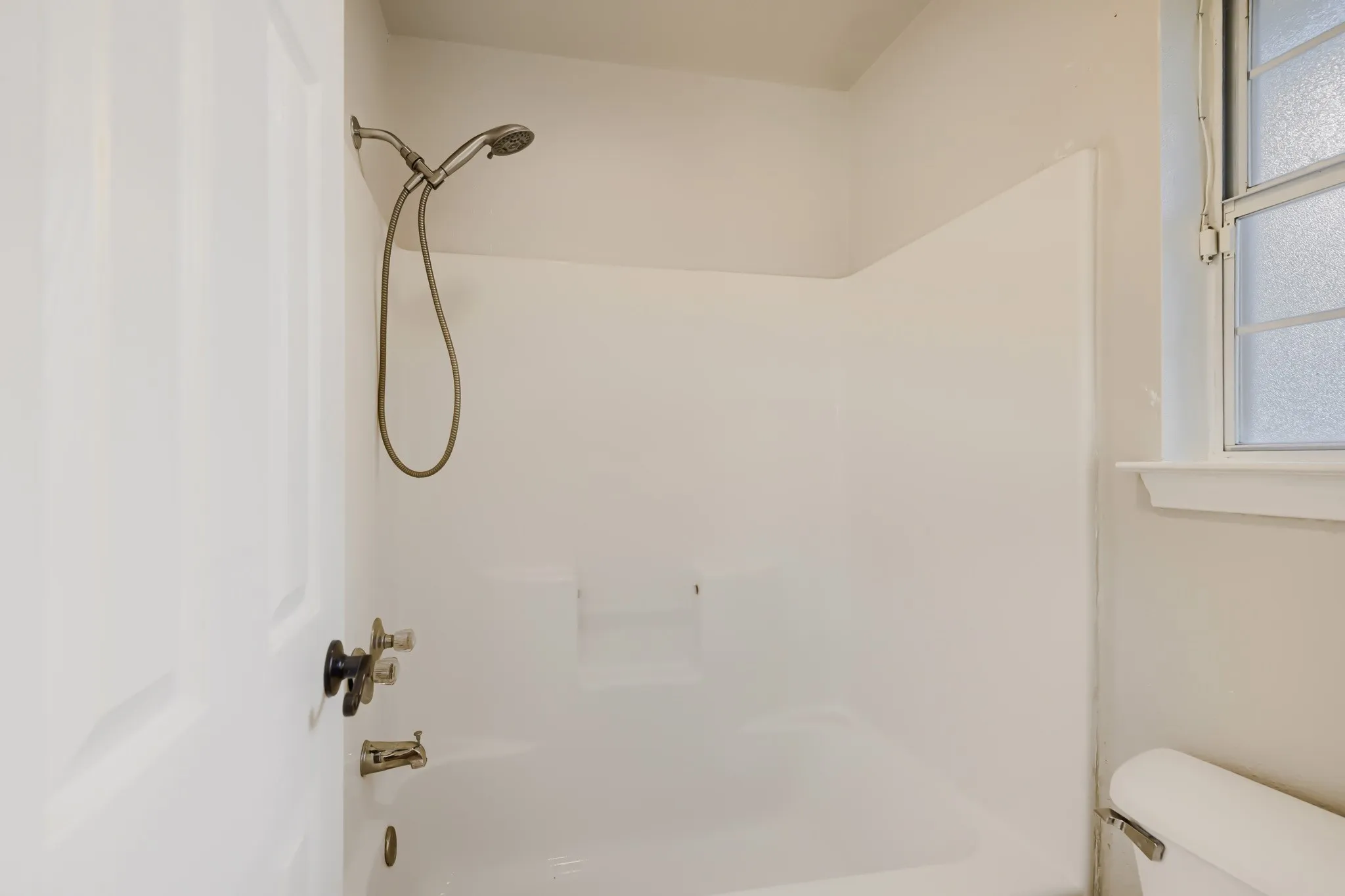 White shower and tub combination with a handheld showerhead and bronze fixtures
