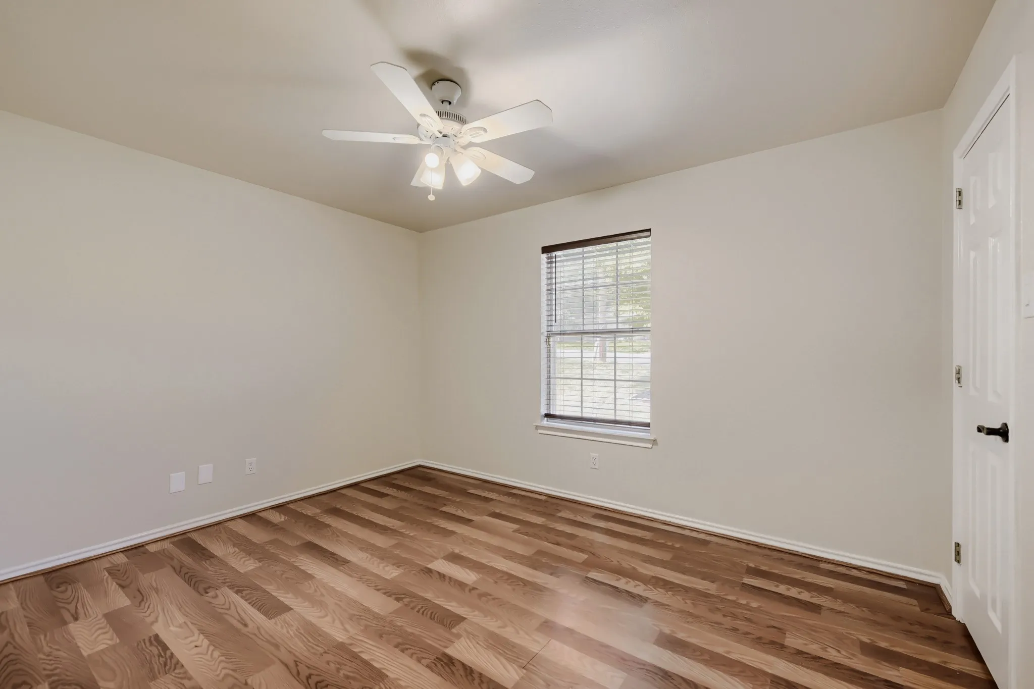 Spacious room featuring wood-finish flooring, a ceiling fan with integrated lighting, and a window with horizontal blinds