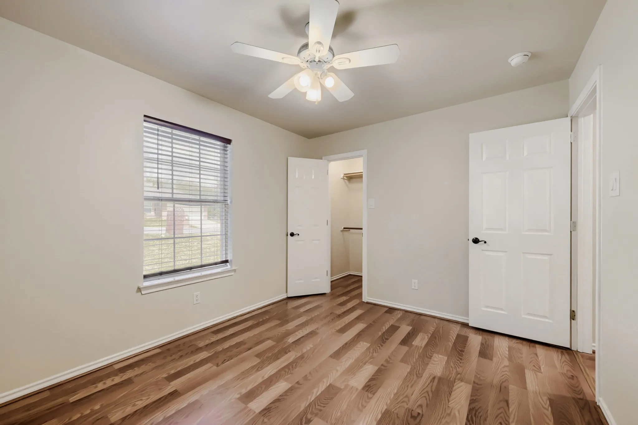 Bedroom featuring wood-finish flooring, a ceiling fan with integrated lighting, a window with horizontal blinds, and a walk-in closet