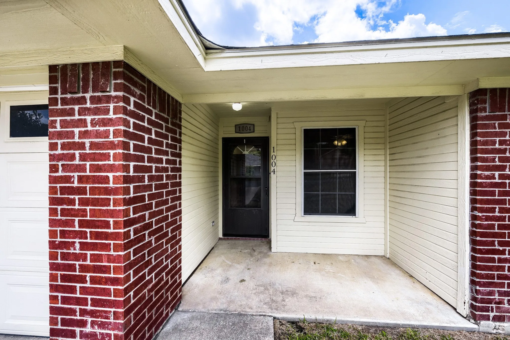 Entryway featuring a covered porch, brick column accents, horizontal siding, and a white garage door
