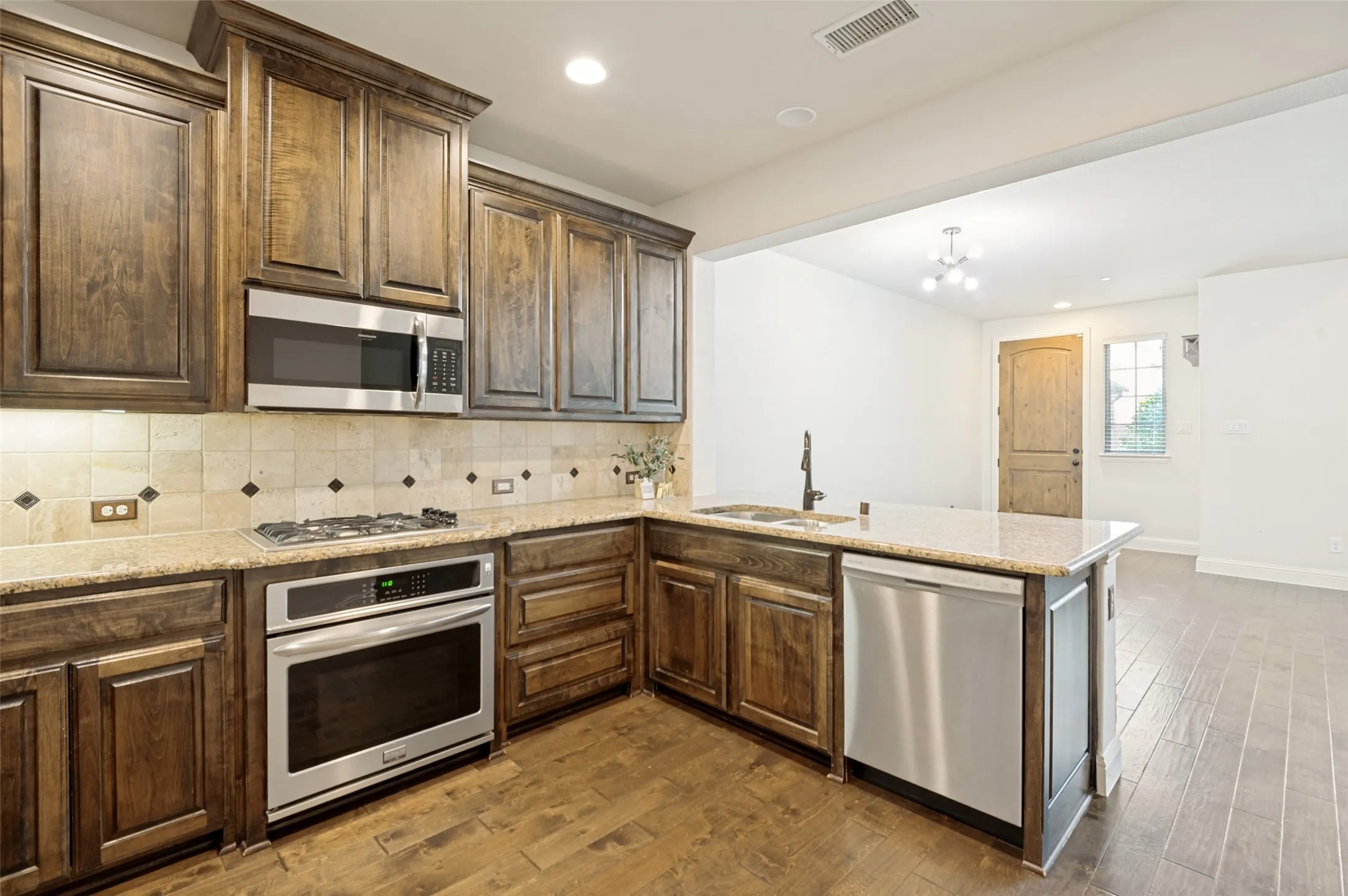 Kitchen featuring dark wood cabinetry, light granite countertops, and stainless steel appliances including a built-in oven, microwave, and dishwasher