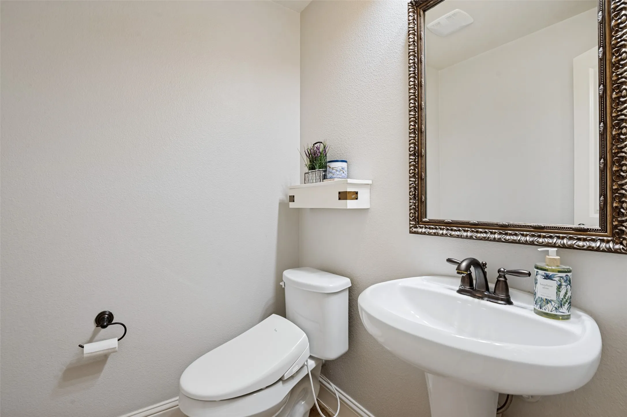 Pedestal sink with bronze-finish faucet, framed mirror, and wall-mounted toilet