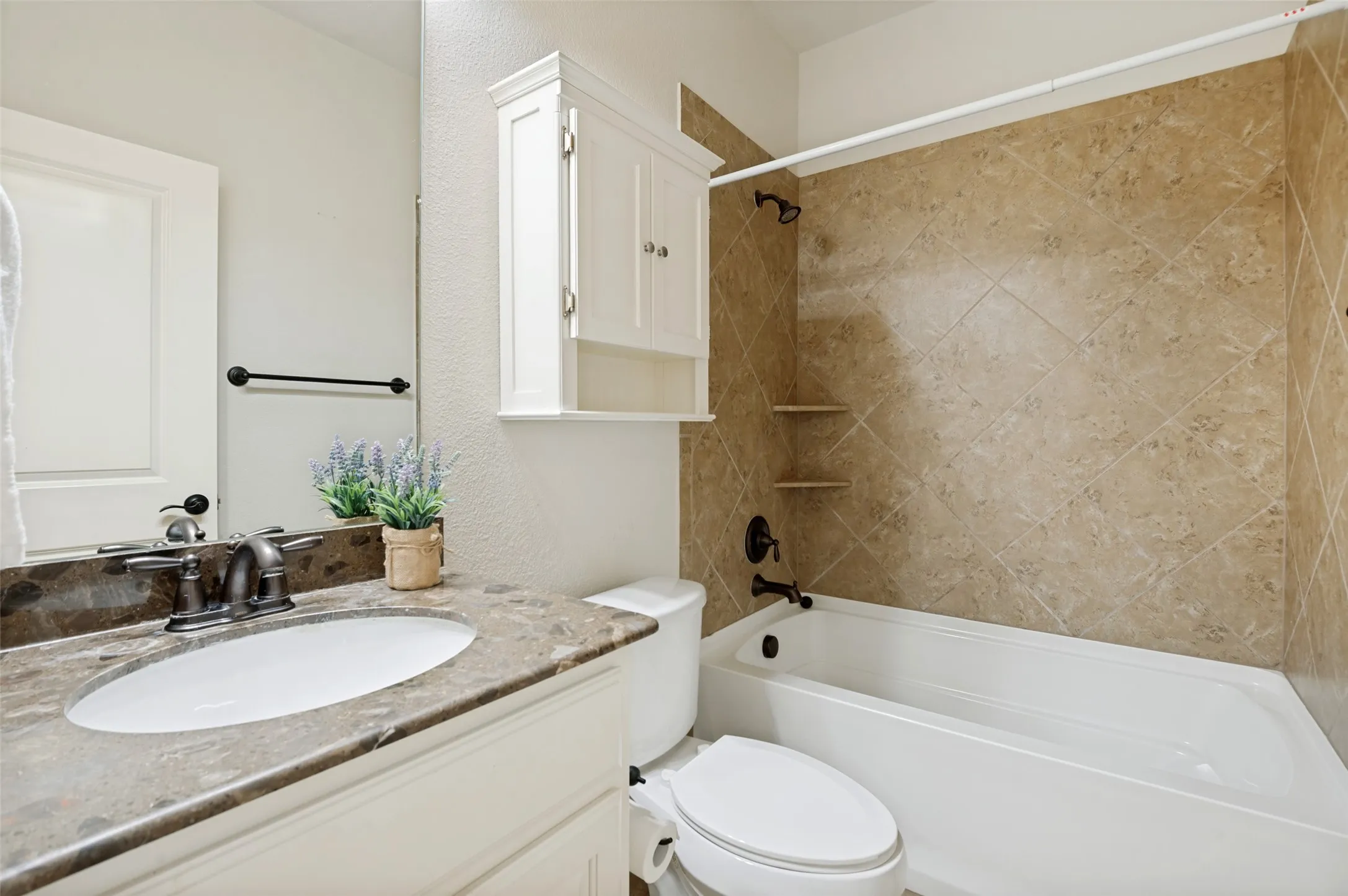 Bathroom featuring a single vanity with a patterned countertop and undermount sink, a white built-in storage cabinet, and a bathtub with full tile surround and oil-rubbed bronze fixtures