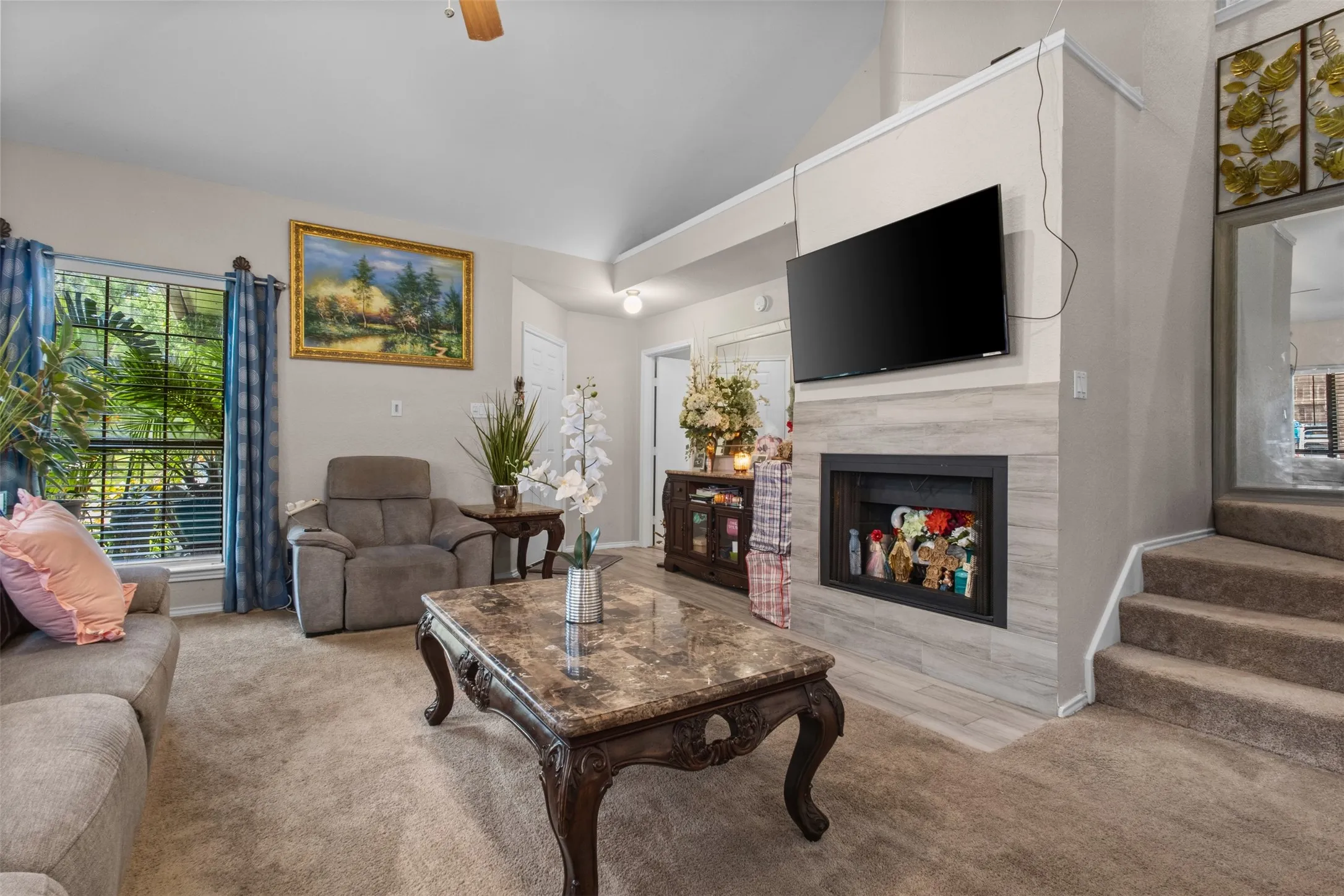 Living area featuring vaulted ceilings, a contemporary fireplace with a stone-look surround, and plush carpet flooring
