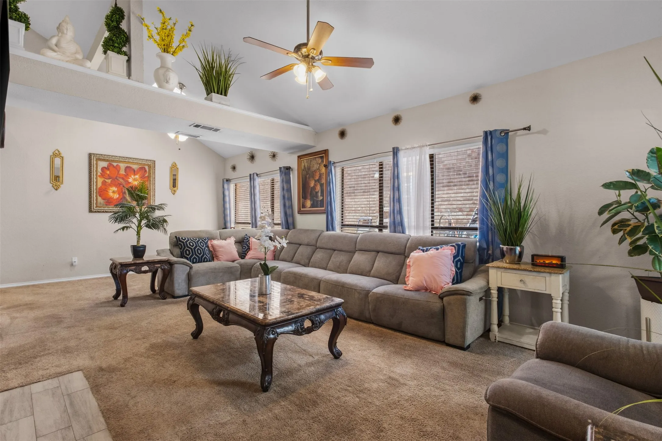 Spacious living area featuring vaulted ceilings, a ceiling fan with integrated lighting, and multiple windows with blinds
