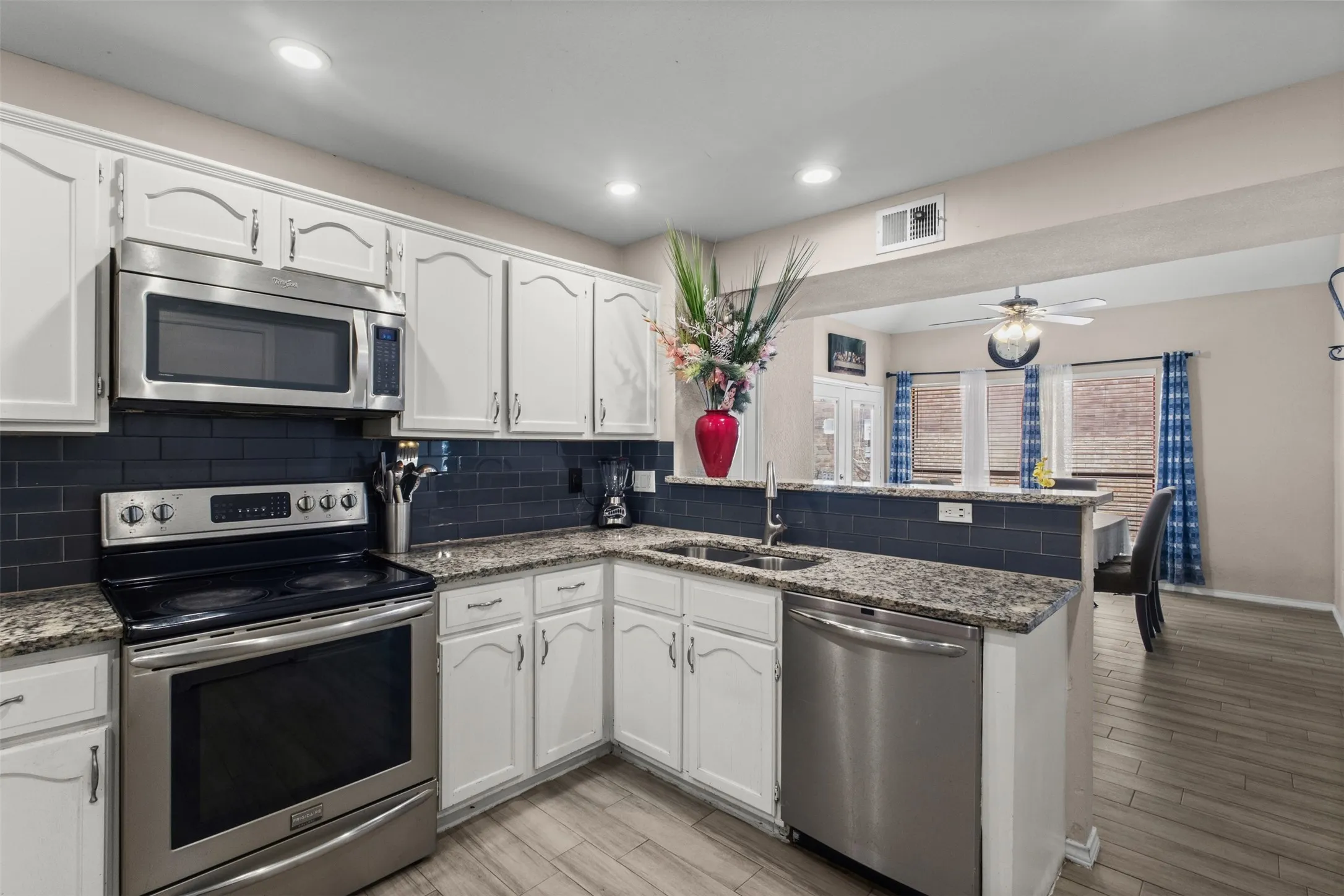 Kitchen featuring white cabinetry, stainless steel appliances, a dark subway tile backsplash, and granite countertops