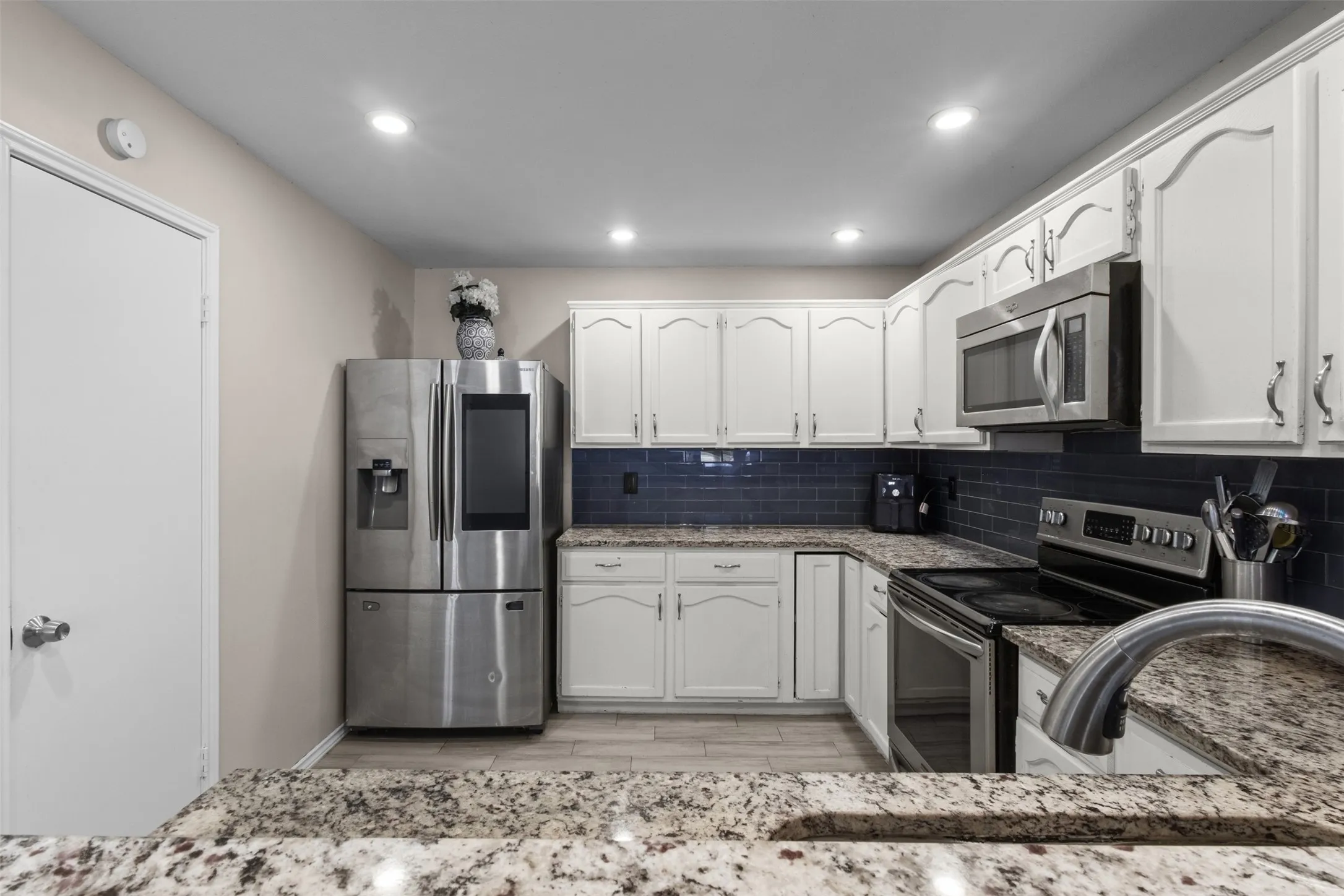 Kitchen featuring light-toned cabinetry, granite countertops, and a dark blue subway tile backsplash