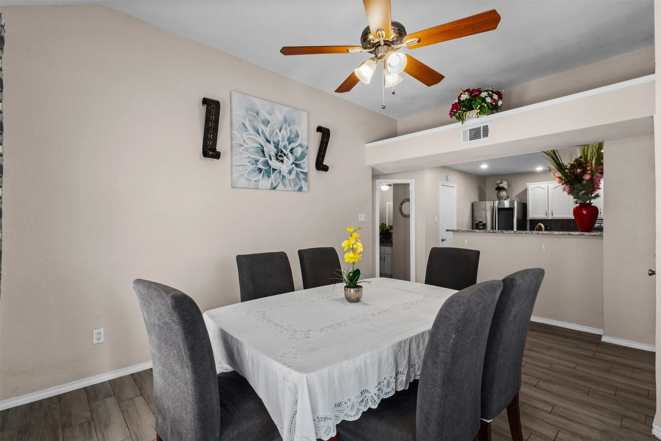 Dining area featuring wood-finish flooring, a ceiling fan with light fixture, and an open pass-through to the kitchen with a granite-style countertop
