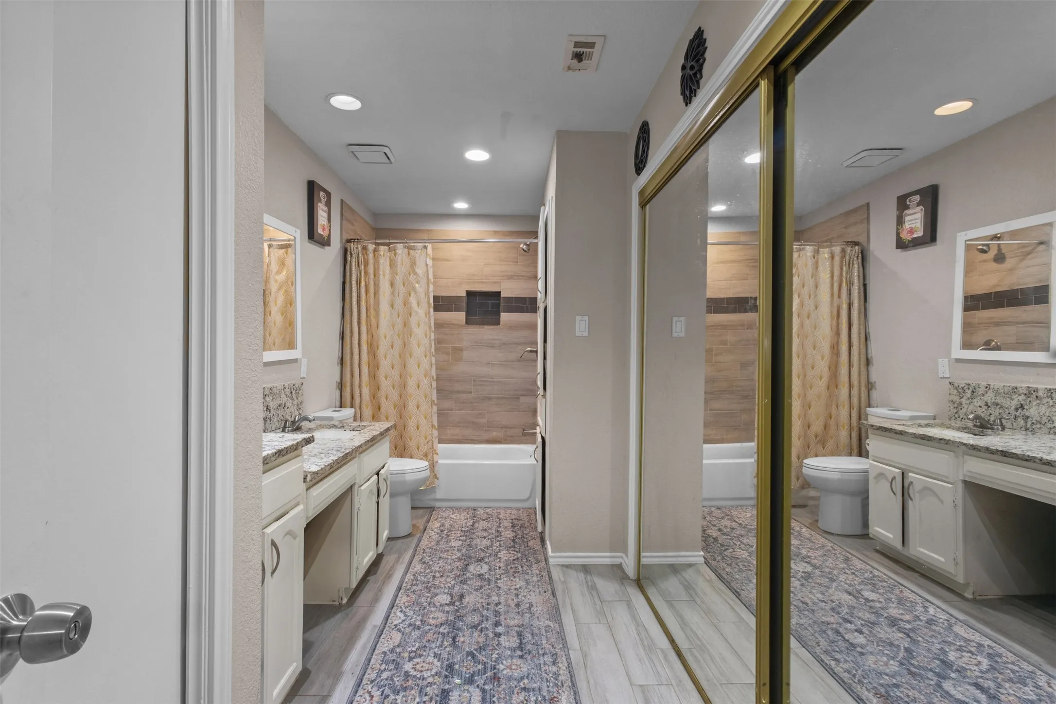 Bathroom featuring dual vanities with light-toned countertops, a full-size bathtub with shower, and wood-finish flooring