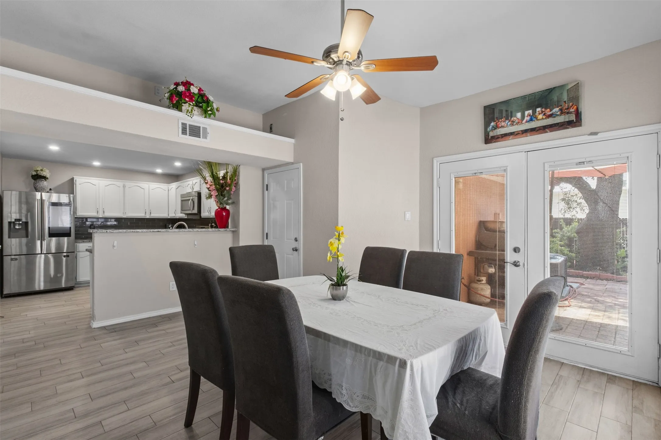 Open-concept dining area featuring wood-finish flooring, a ceiling fan, and double glass-paneled doors leading to an outdoor patio