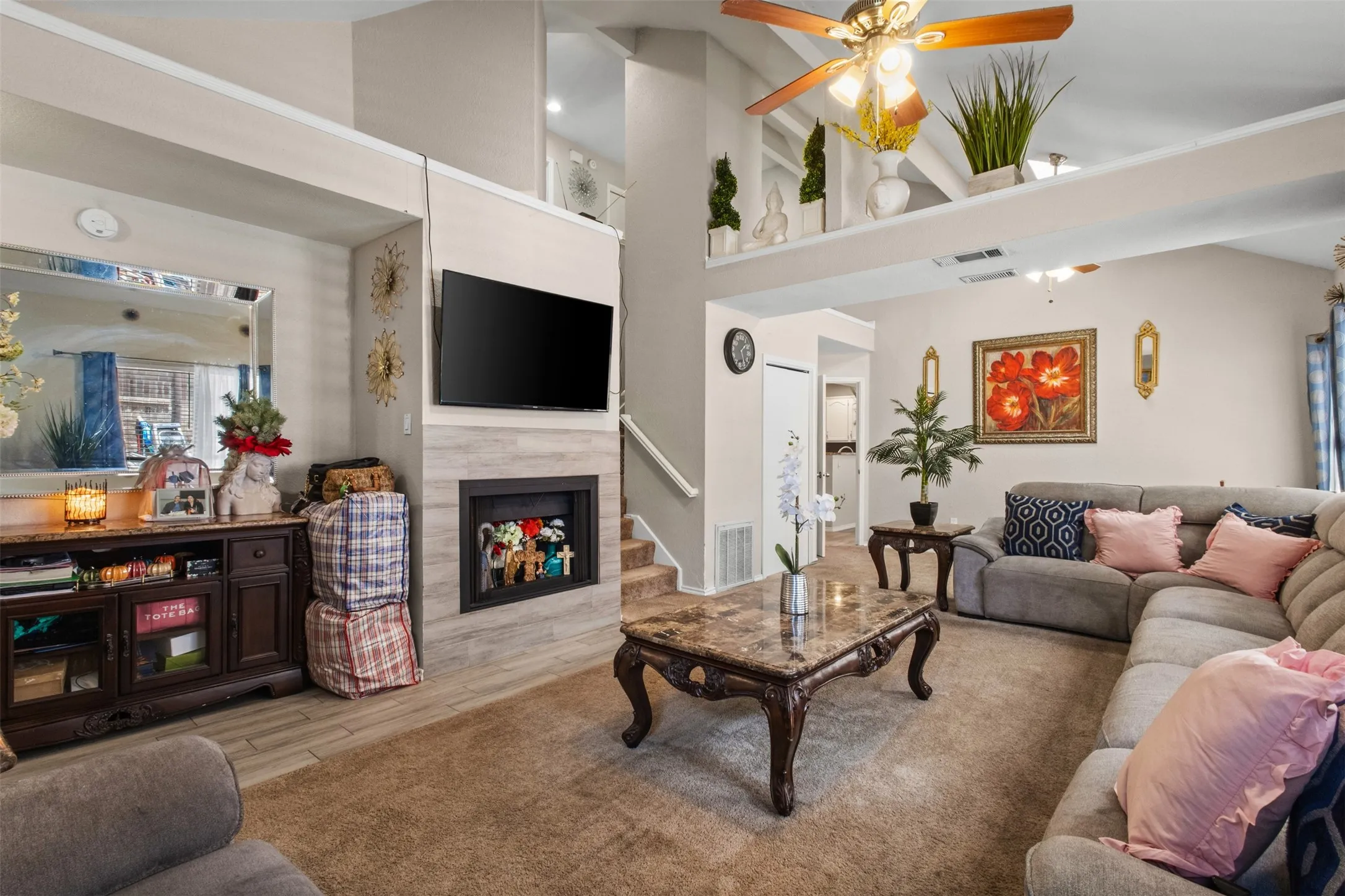 Spacious living area featuring a fireplace with a light wood-finish surround, vaulted ceilings, a ceiling fan, and carpet flooring