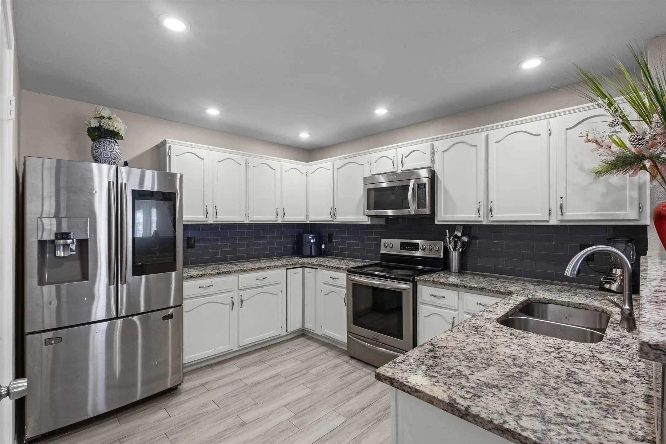 Modern kitchen featuring light wood-finish flooring, white cabinetry with dark hardware, dark subway tile backsplash, and light speckled countertops