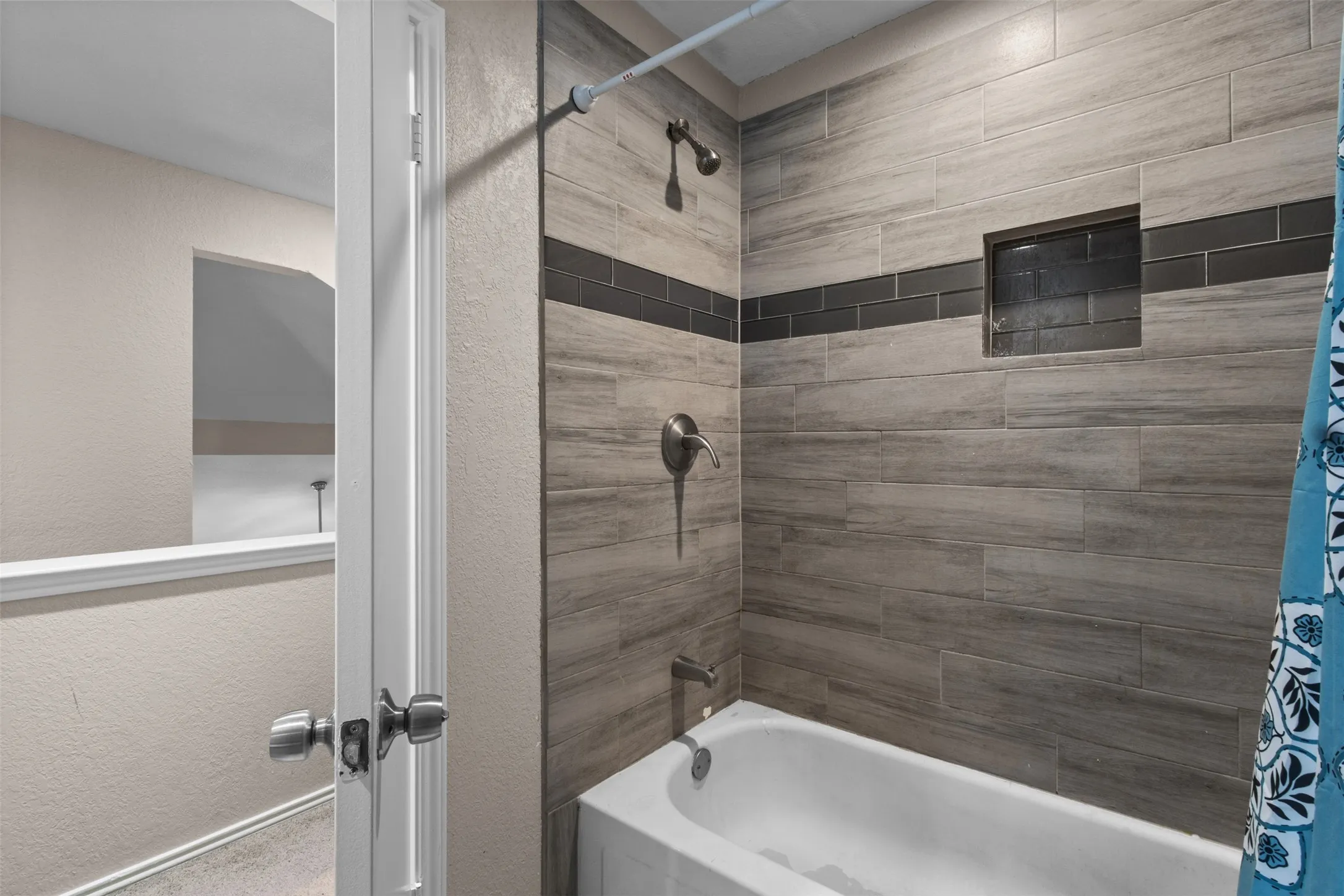 Bathtub with a tiled surround featuring wood-look porcelain tiles and a contrasting dark subway tile accent band