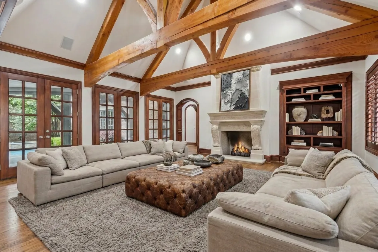Vaulted ceiling with exposed wood beams, stone fireplace, built-in shelving, wood-finish French doors, and wood-finish flooring