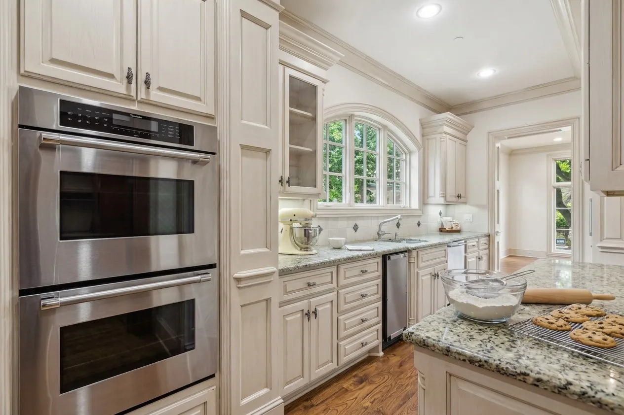 AI painted scullery Gourmet kitchen featuring stainless steel double ovens, custom cabinetry, granite countertops, an arched window, and wood-finish flooring