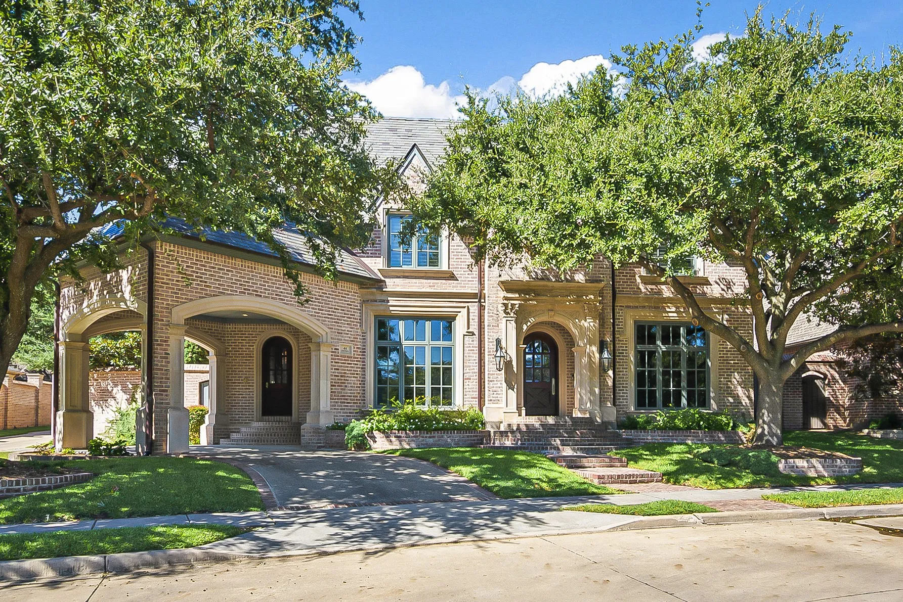 Brick exterior with stone accents, arched porte-cochère, decorative entry door, and manicured landscaping