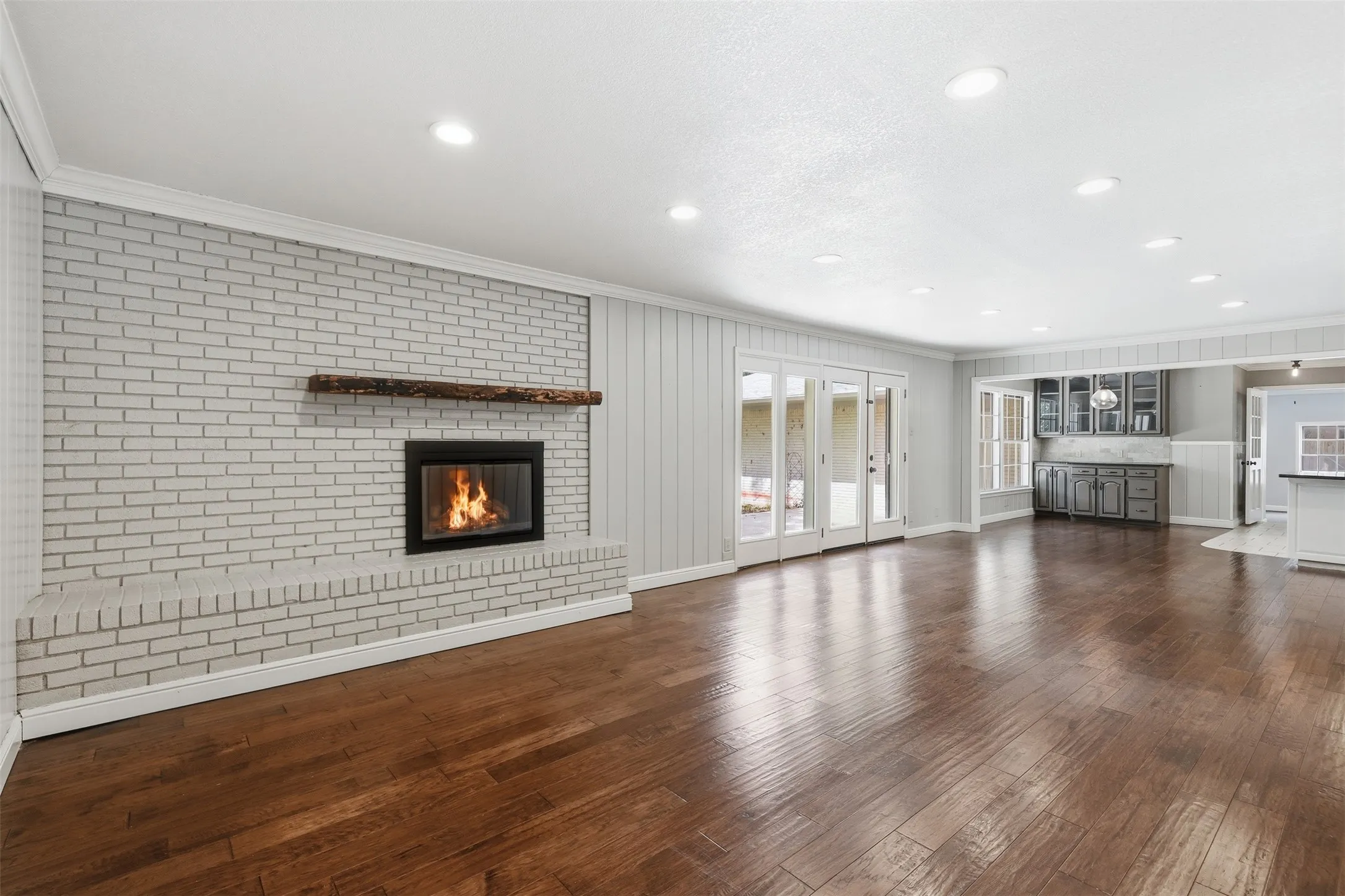 Spacious living area featuring a white brick fireplace with a wood mantel, rich wood-finish flooring, recessed lighting, and French doors leading outdoors