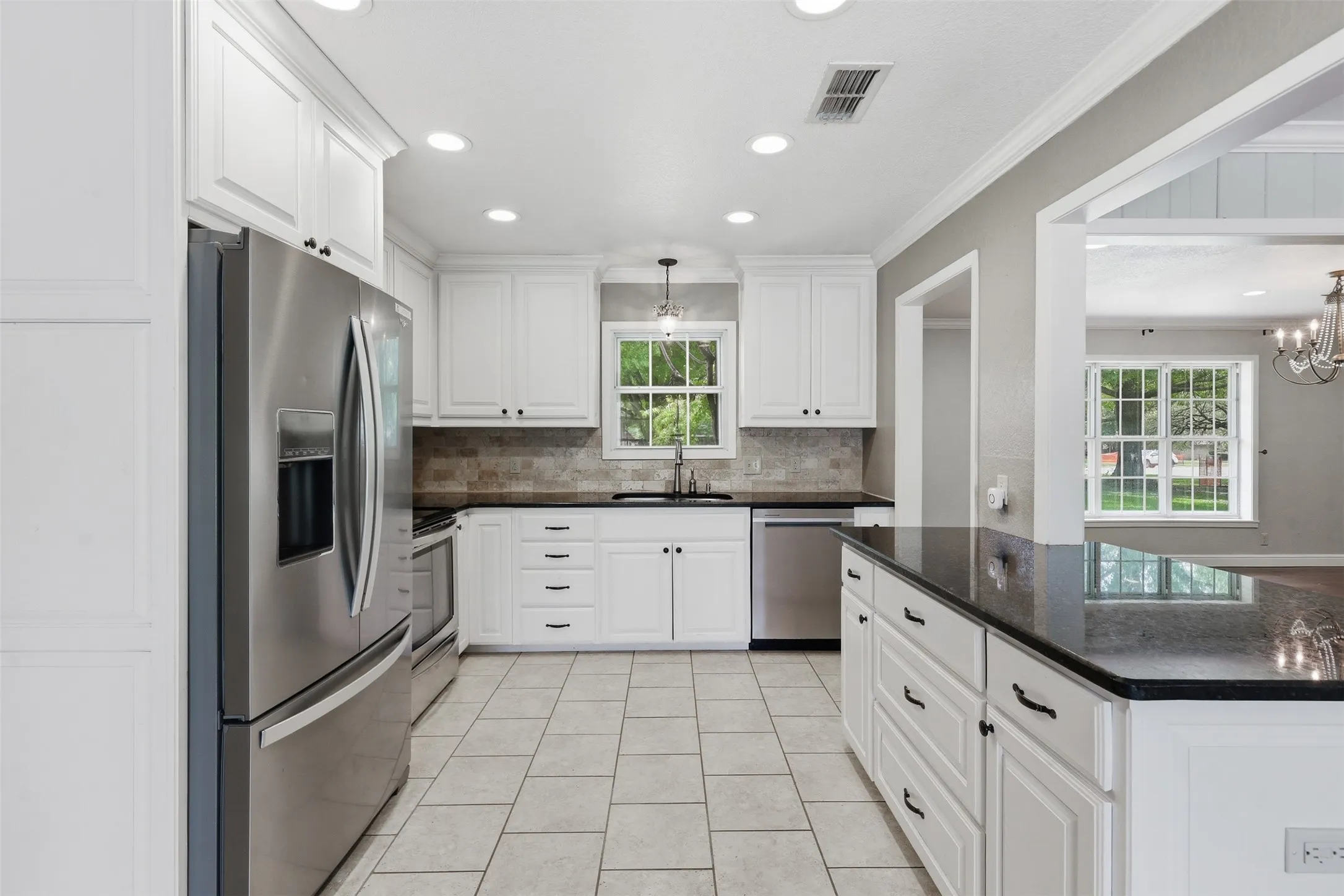Bright kitchen featuring white cabinetry, dark countertops, stainless steel appliances, a tile backsplash, and recessed lighting