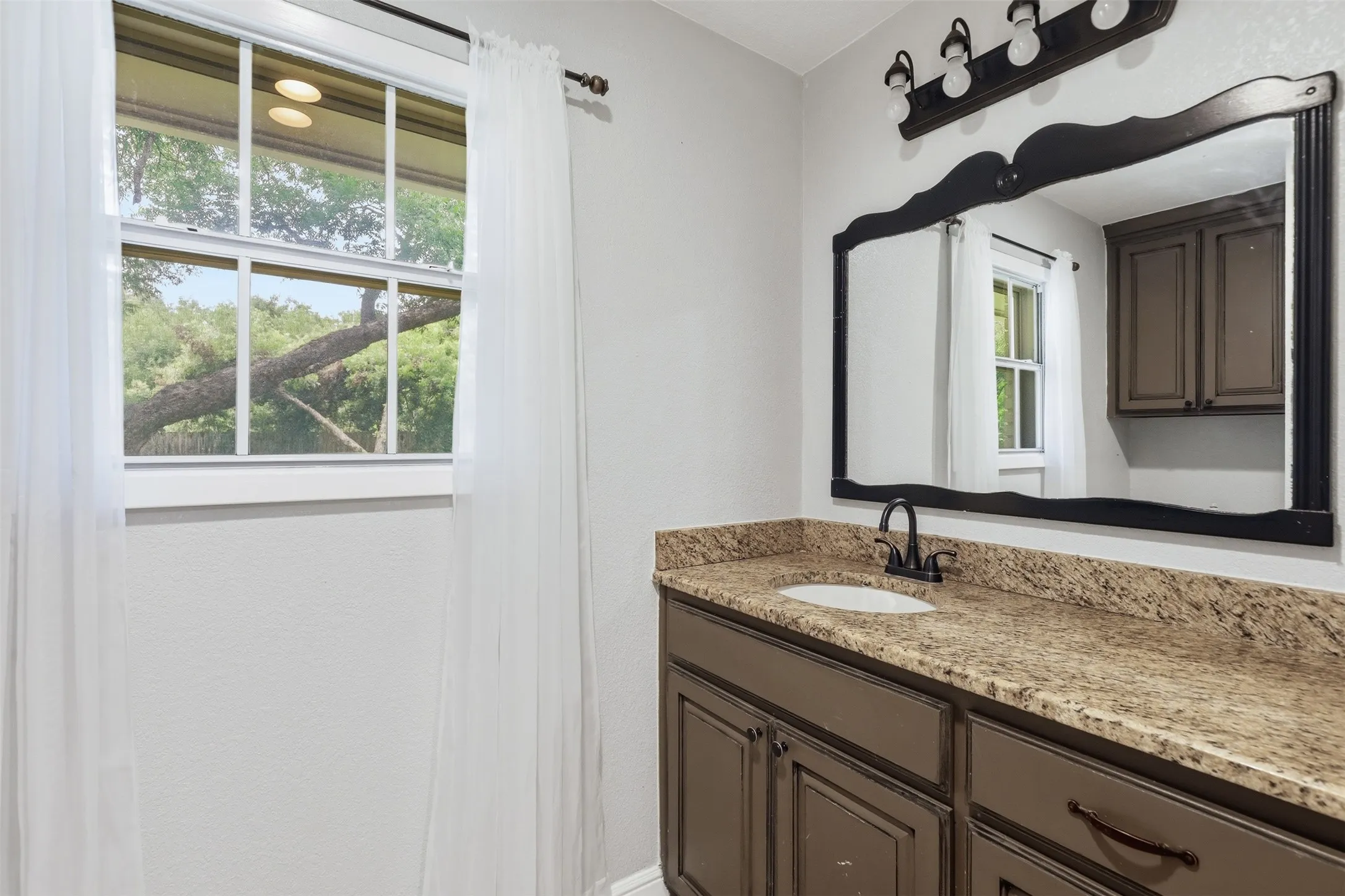Bathroom vanity with a brown cabinet base, speckled countertop, and an undermount sink with a dark-finish faucet