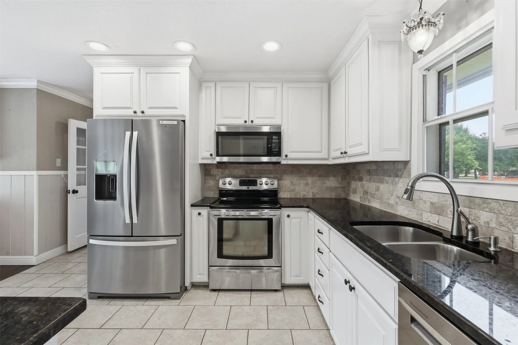 Kitchen featuring white upper and lower cabinetry, dark stone countertops, stainless steel appliances, and a mosaic tile backsplash