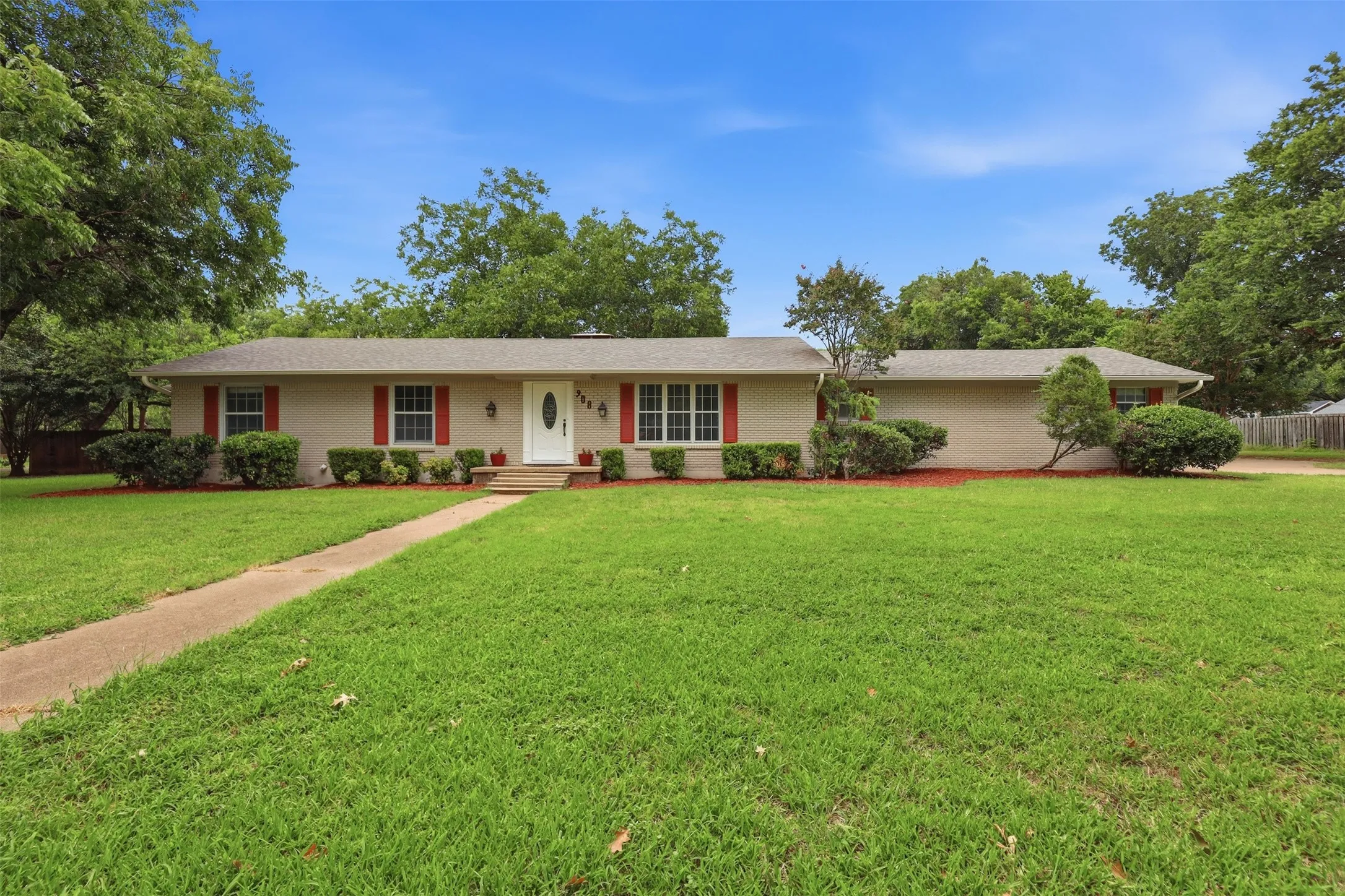 Ranch-style residence featuring a light-toned brick facade, a symmetrical white front door, and red decorative shutters