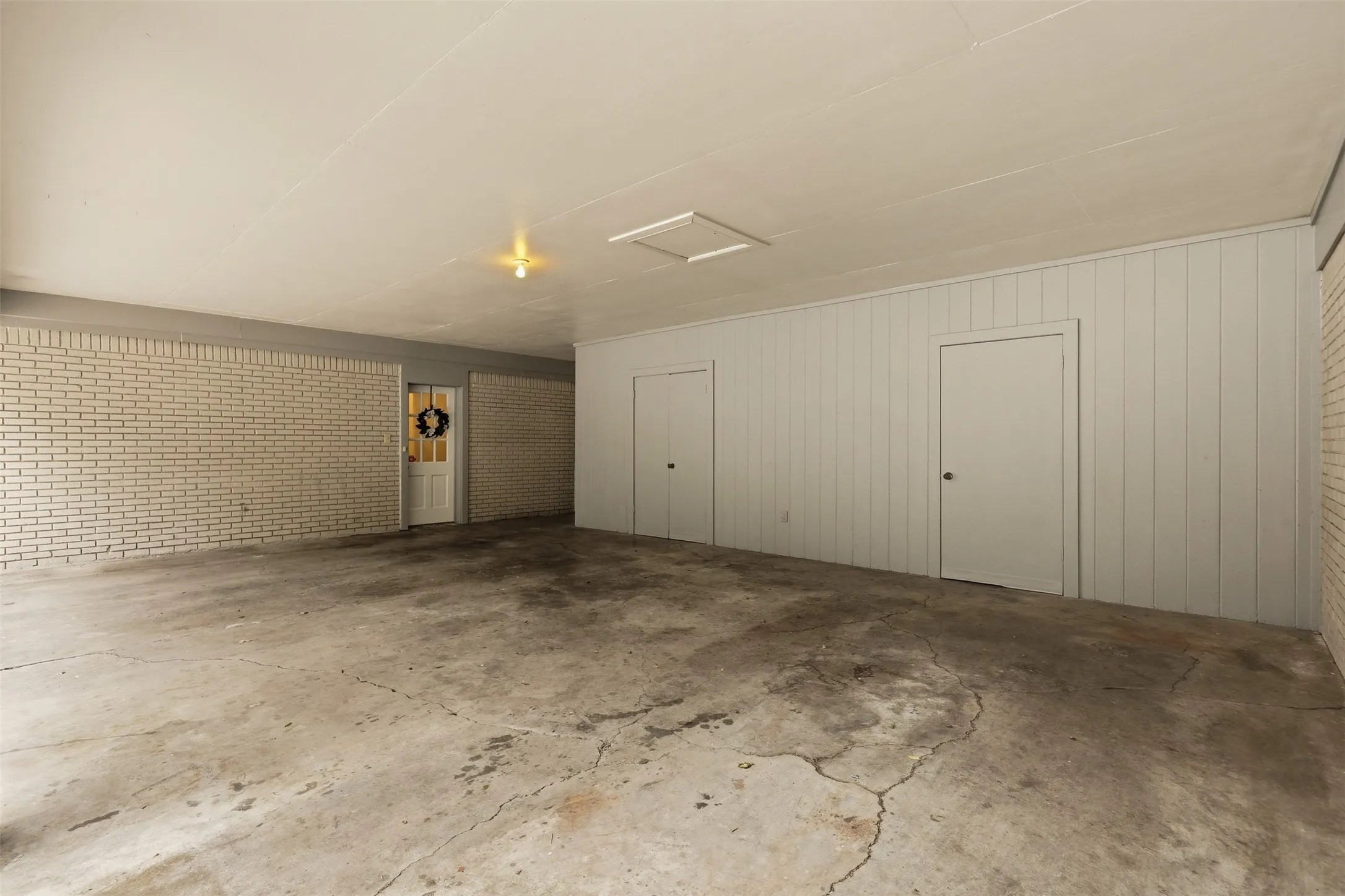 Spacious covered area featuring concrete flooring, a light brick wall, and two panel doors