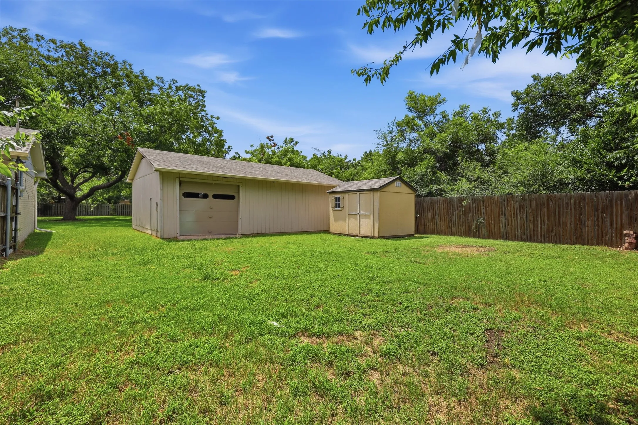 Expansive backyard featuring a detached garage with a roll-up door, a separate storage shed, and a privacy fence