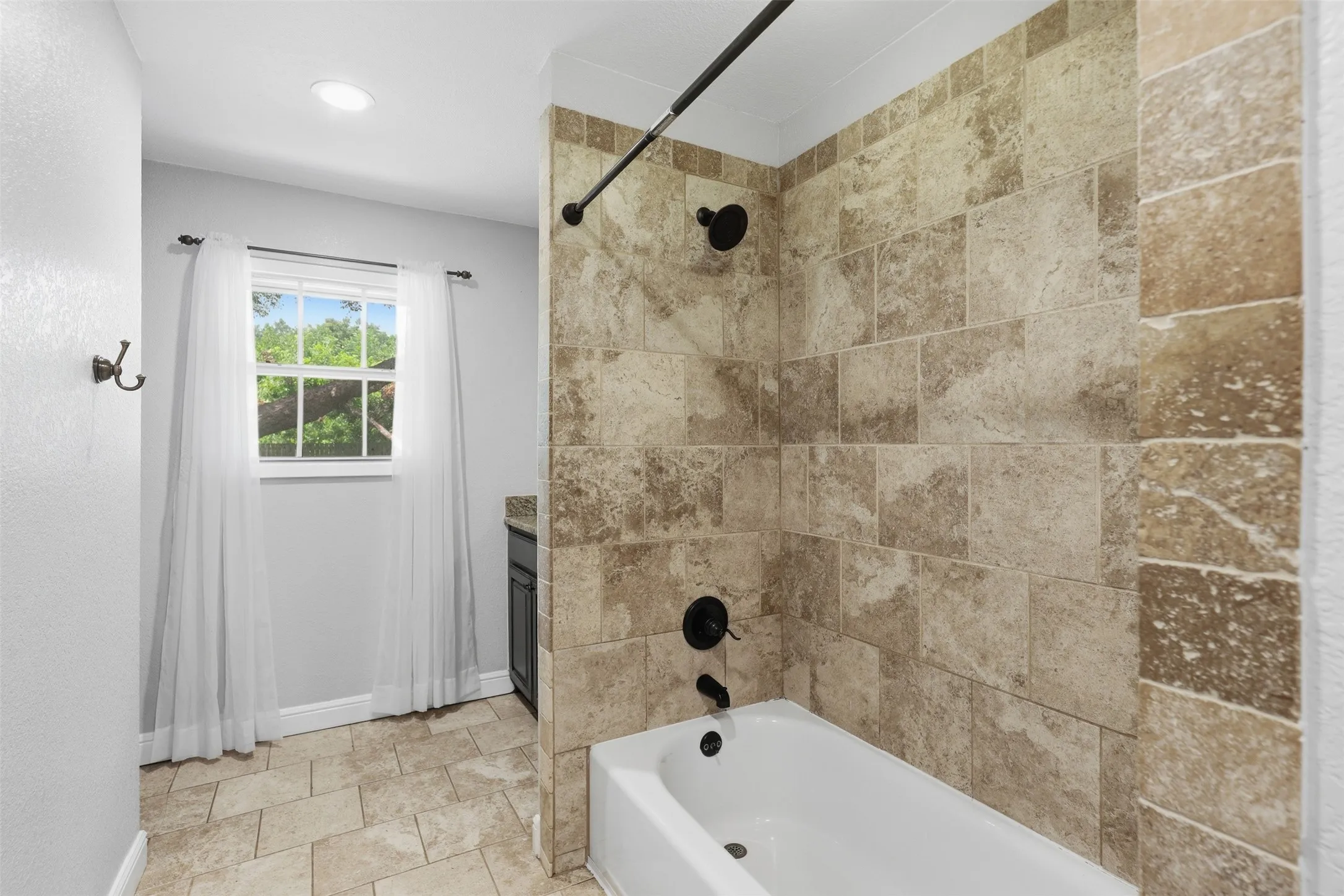Tiled bath and shower combination featuring black fixtures and a window with white sheers
