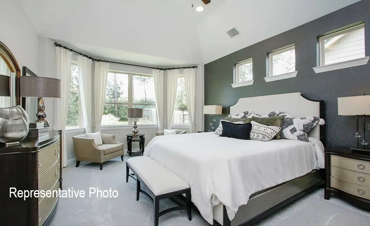 Spacious bedroom featuring a vaulted ceiling, bay window, light grey carpeting, and a dark accent wall