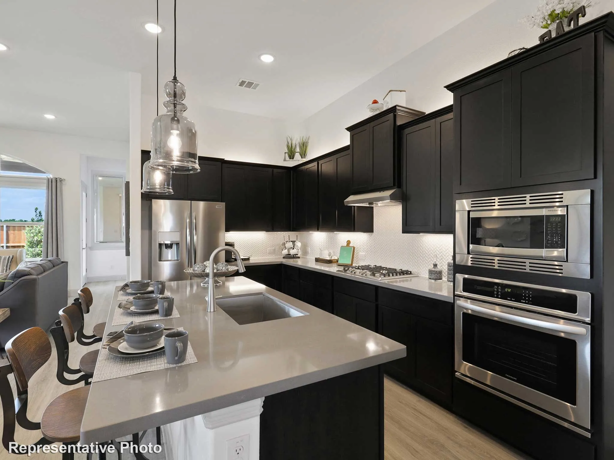 Modern kitchen featuring dark cabinetry, stainless steel appliances, a center island with sink, and pendant lighting
