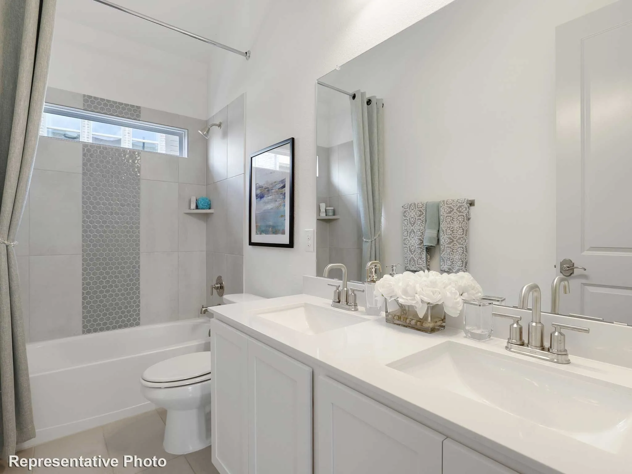 Bathroom featuring a dual vanity with undermount sinks and brushed nickel fixtures, a full-width mirror, a tub/shower combination with light-toned tiling and a mosaic accent, and a horizontal transom window
