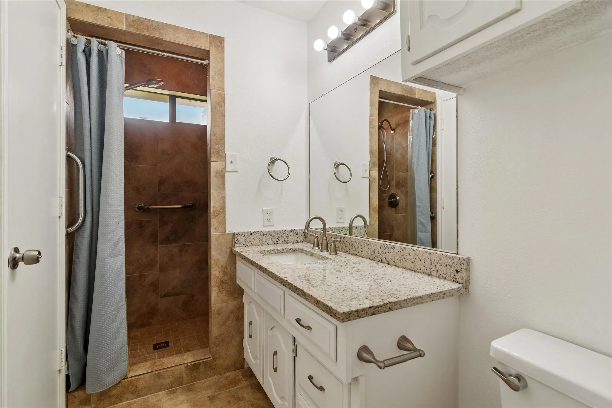Bathroom featuring a white vanity with a speckled countertop, undermount sink, and brushed nickel faucet