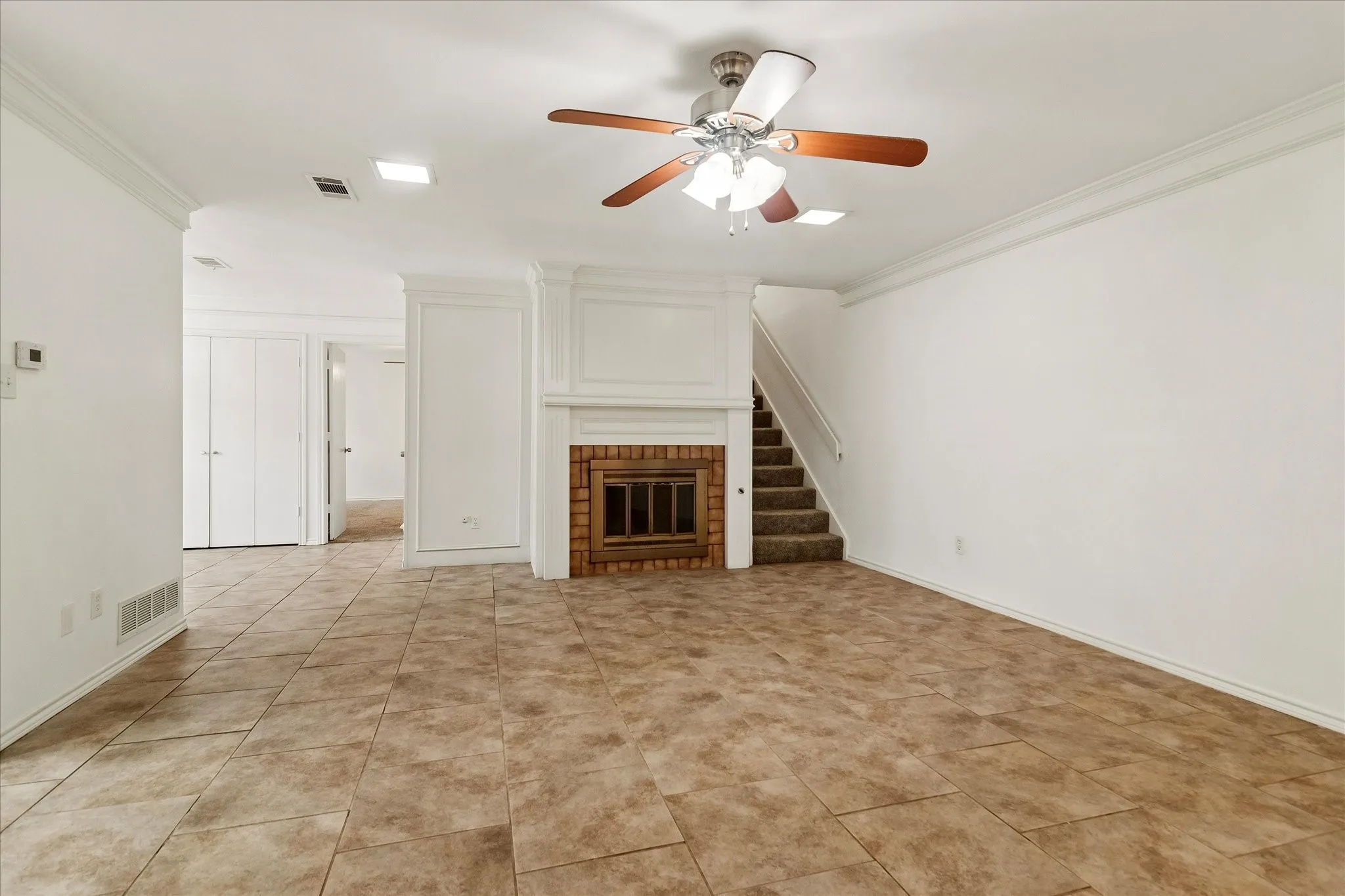 Spacious living area featuring neutral tile flooring, a wood-burning fireplace with brick surround, and a ceiling fan with integrated lighting