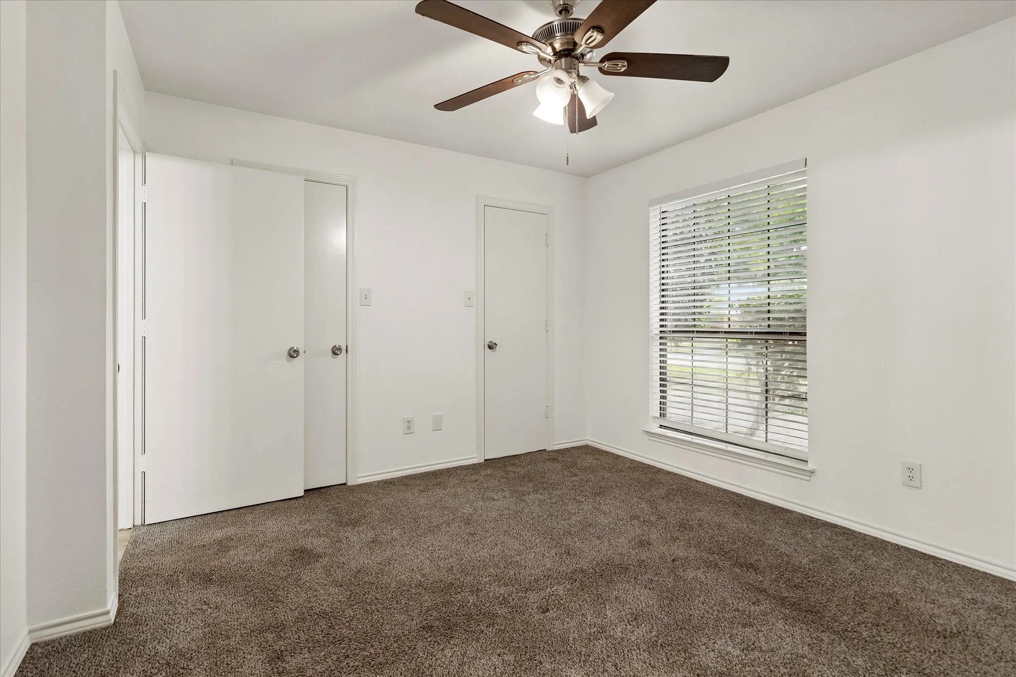 Carpeted interior space featuring a ceiling fan with integrated lighting, a window with horizontal blinds, and white interior doors with round knob hardware