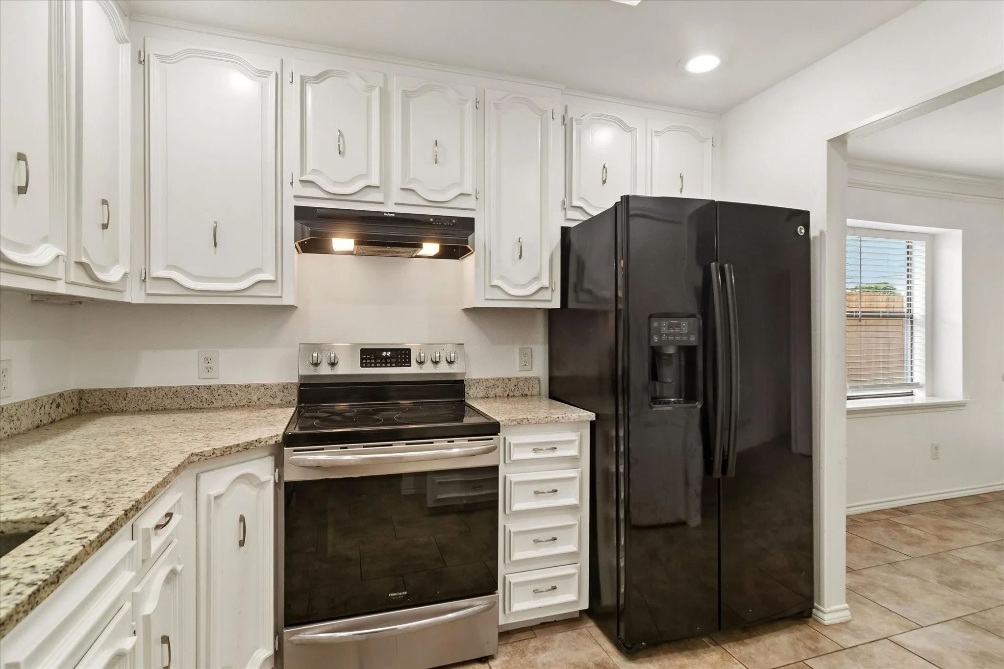 Kitchen featuring white cabinetry, light-toned countertops, a stainless steel range with an overhead vent, and a black side-by-side refrigerator