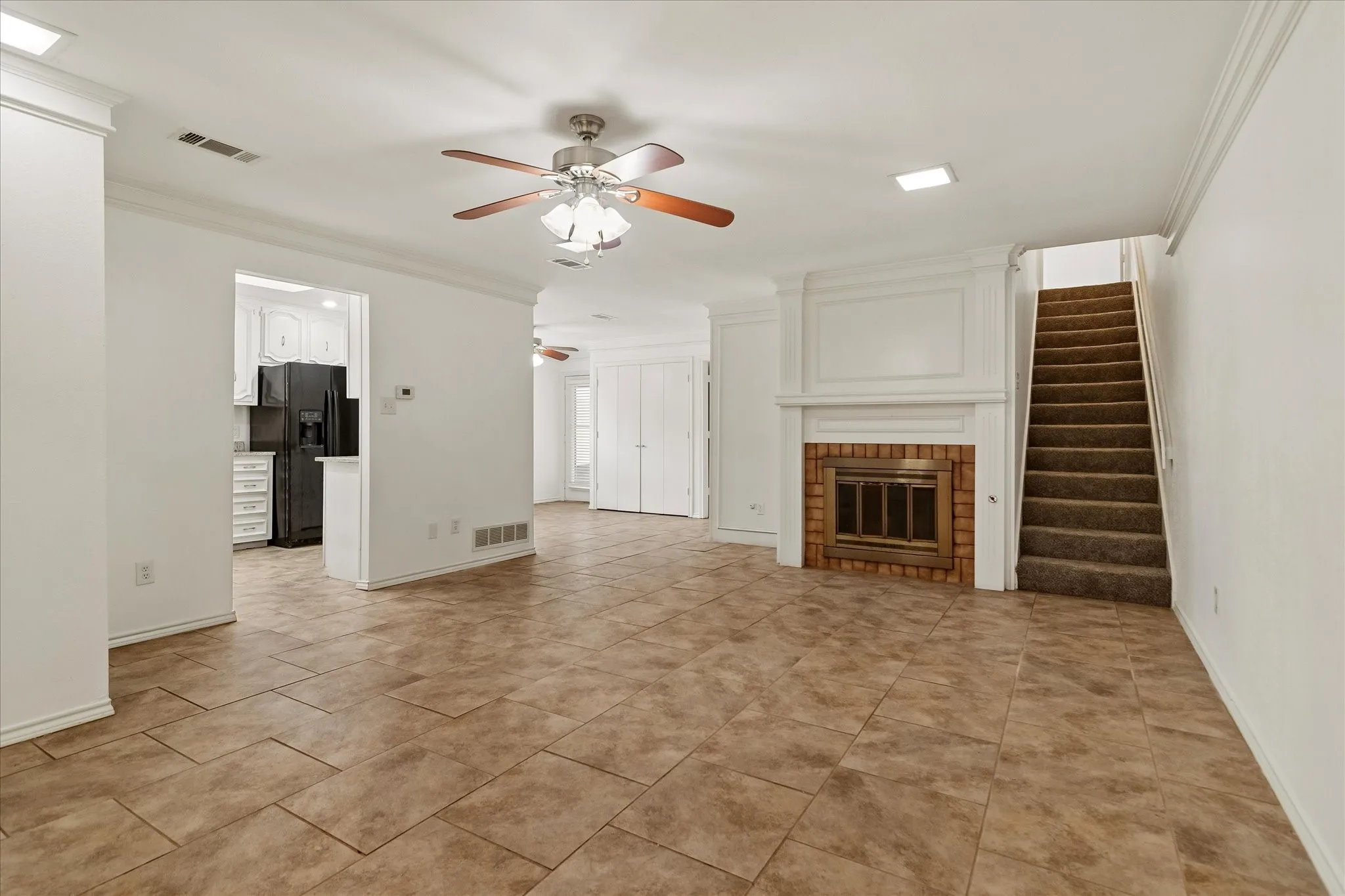 Open-concept living space featuring large format tile flooring, a white-painted fireplace with brick surround, and a ceiling fan