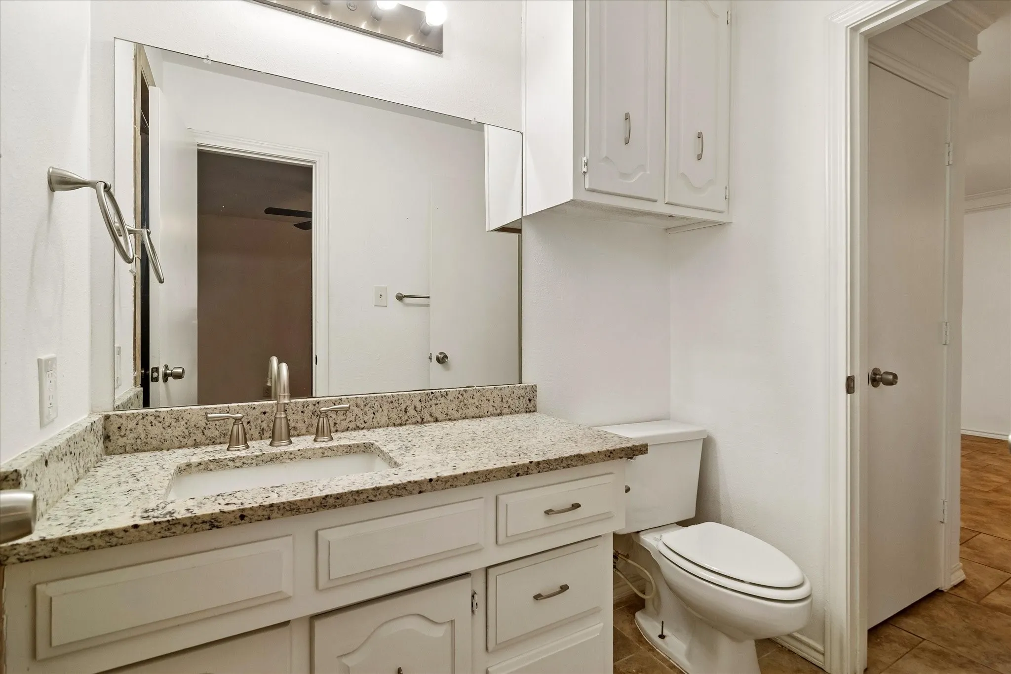Bathroom featuring a white vanity with recessed panel cabinetry, a light speckled countertop, an undermount sink, and a large wall-mounted mirror