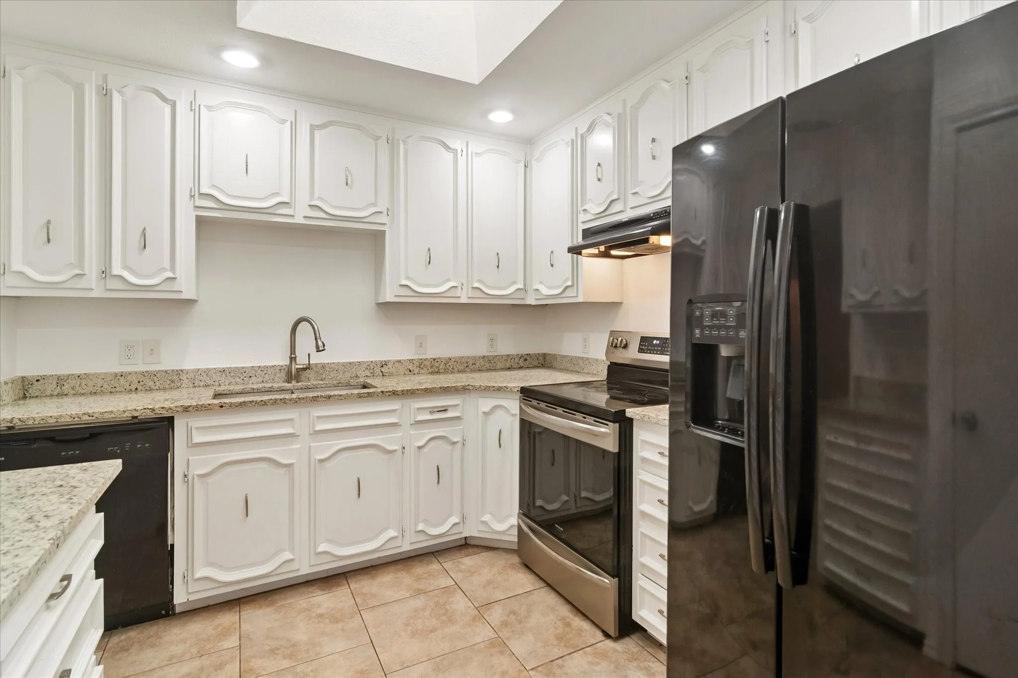 Kitchen featuring white cabinetry, light-toned granite countertops, stainless steel appliances, a black refrigerator, and tiled flooring