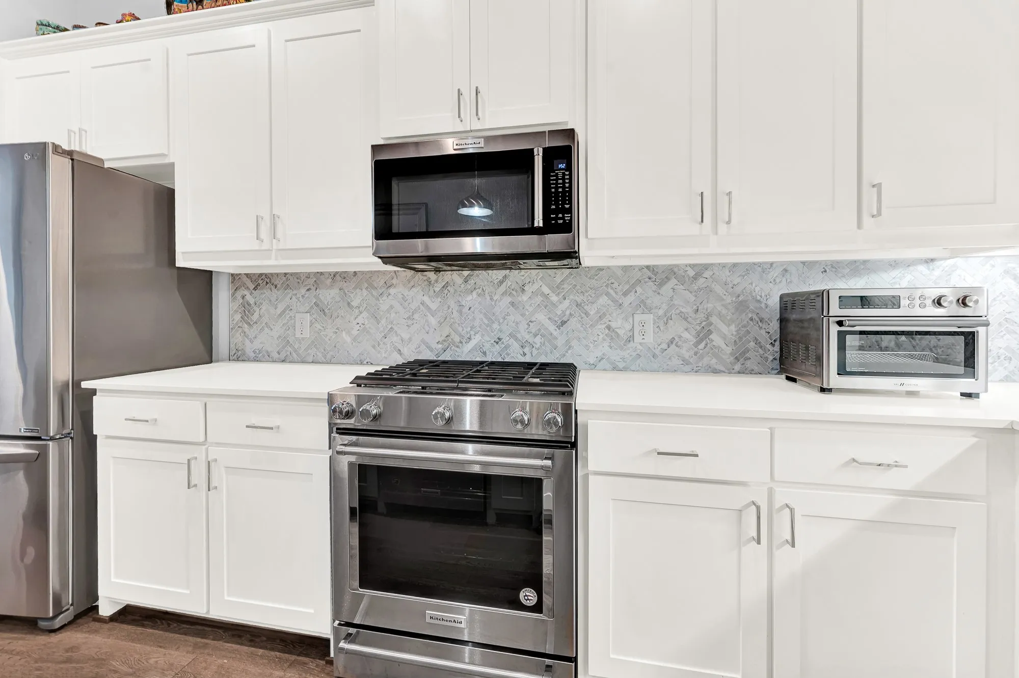 Kitchen featuring white shaker cabinetry, white countertops, a herringbone pattern tile backsplash, and stainless steel appliances including a range, gas cooktop and microwave