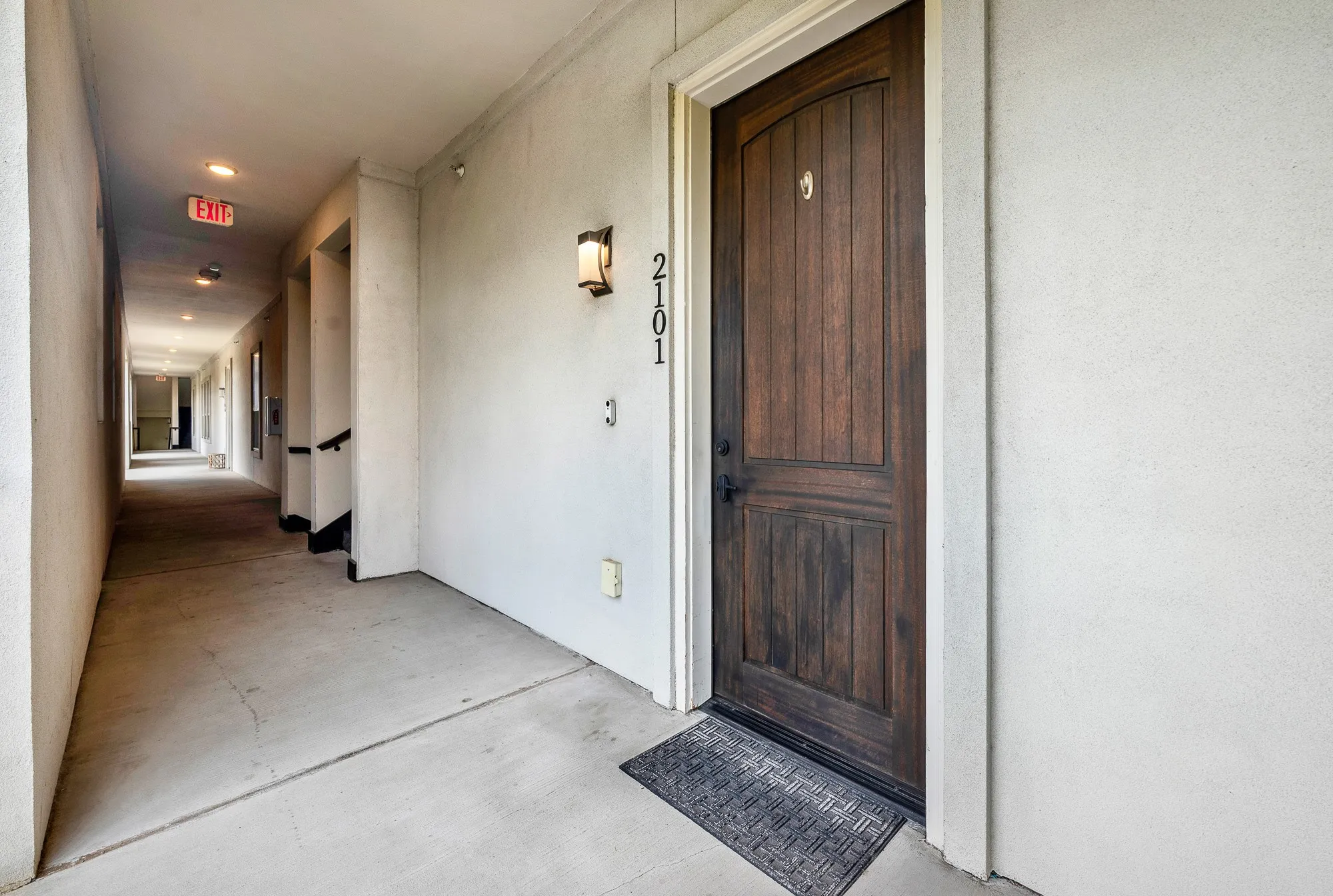 Rich wood-paneled entry door featuring dark iron hardware, illuminated by an exterior sconce
