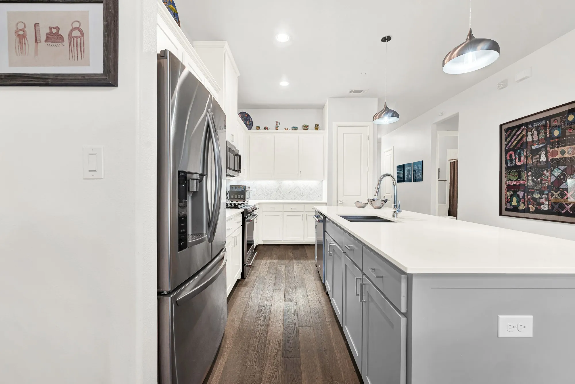 Modern kitchen featuring a large center island with a built-in sink and pendant lighting, stainless steel appliances, white cabinetry, a tiled backsplash, and wood-finish flooring