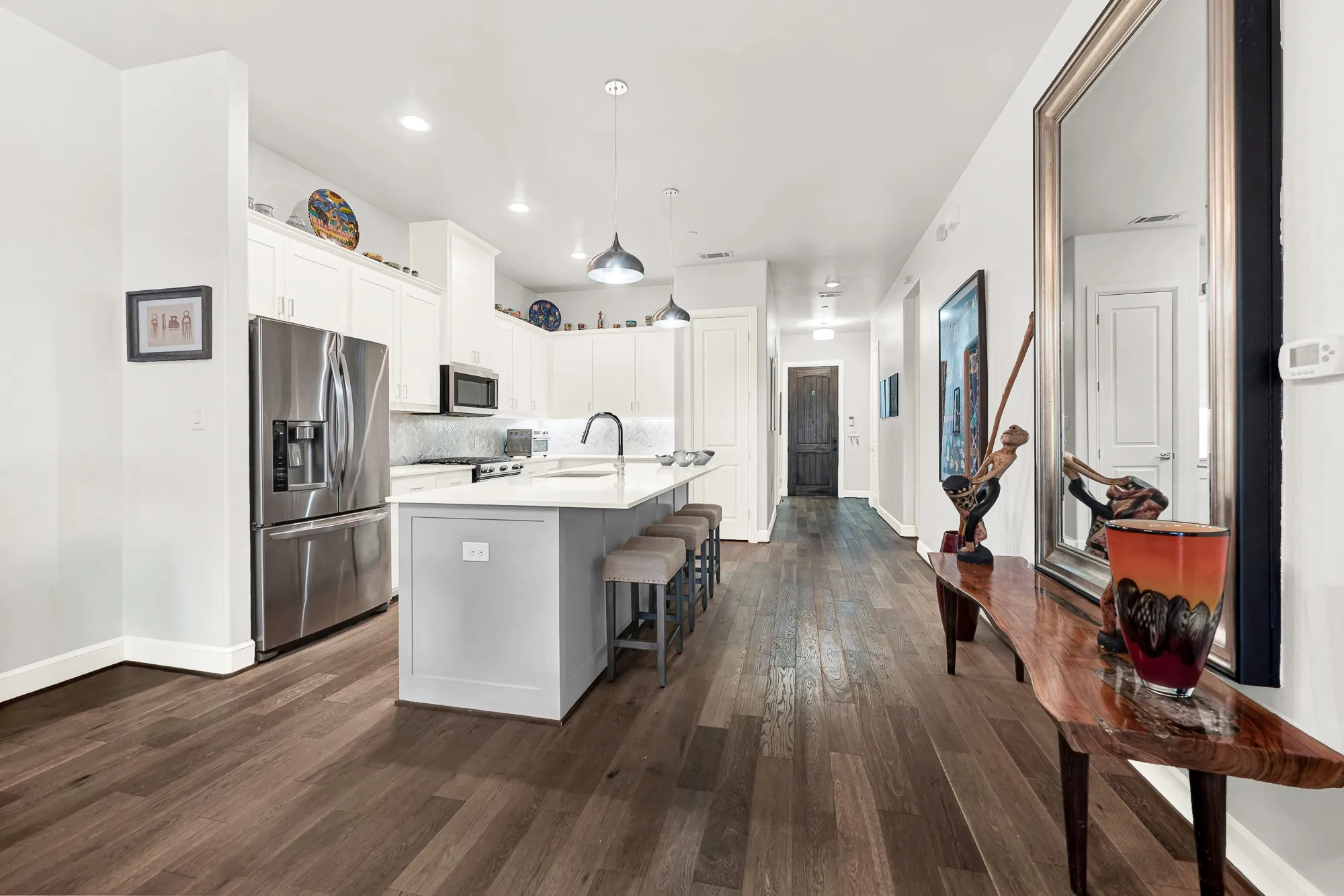 Spacious kitchen featuring an expansive center island with seating, stainless steel appliances, white cabinetry, and a subway tile backsplash