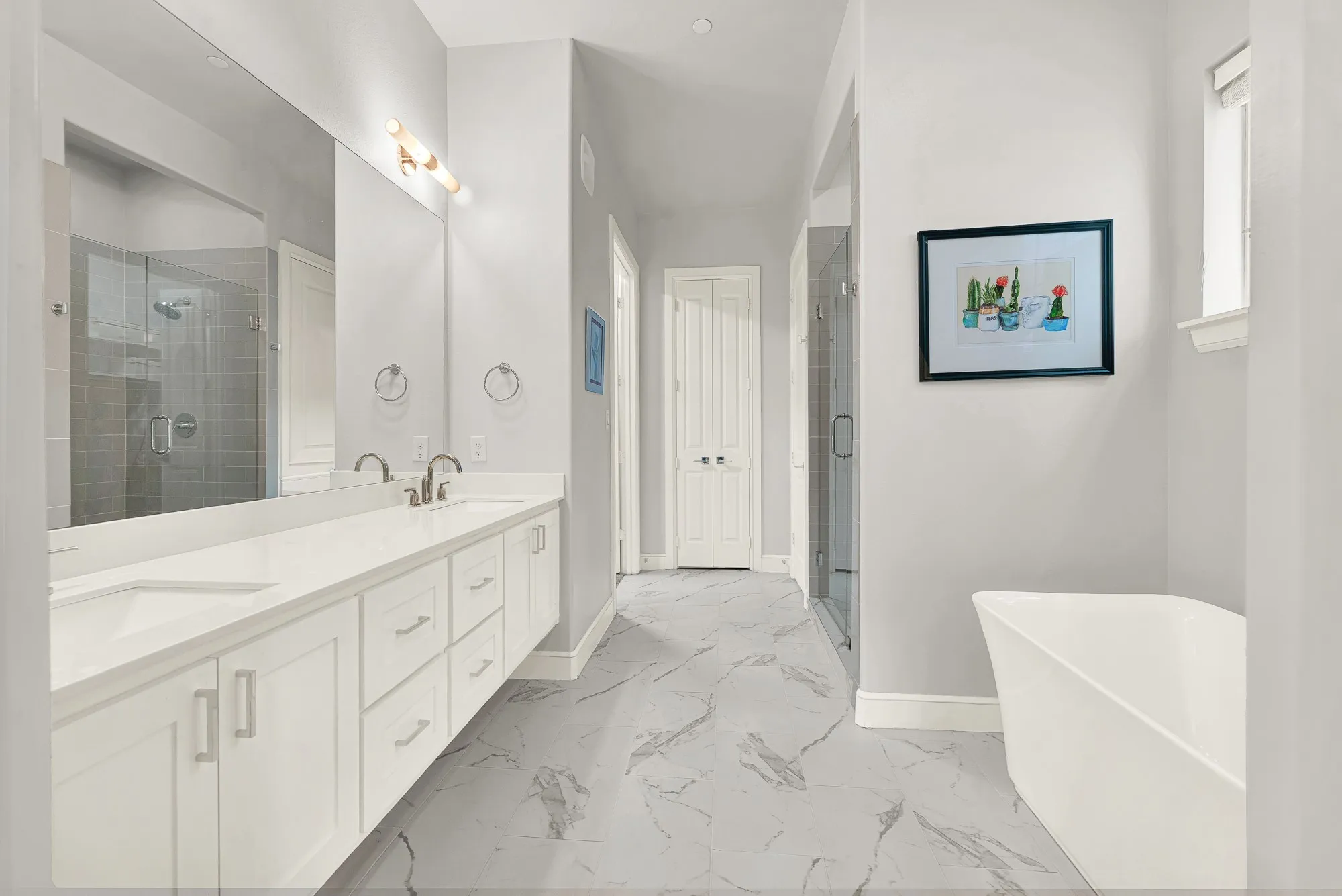 Spacious bathroom featuring a dual vanity with white cabinetry and light-colored countertops, an oversized mirror, and a freestanding soaking tub