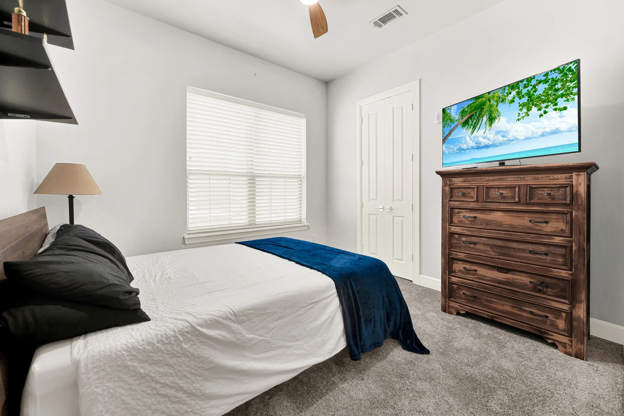 Carpeted bedroom featuring a large window with horizontal blinds, a ceiling fan, and a paneled door