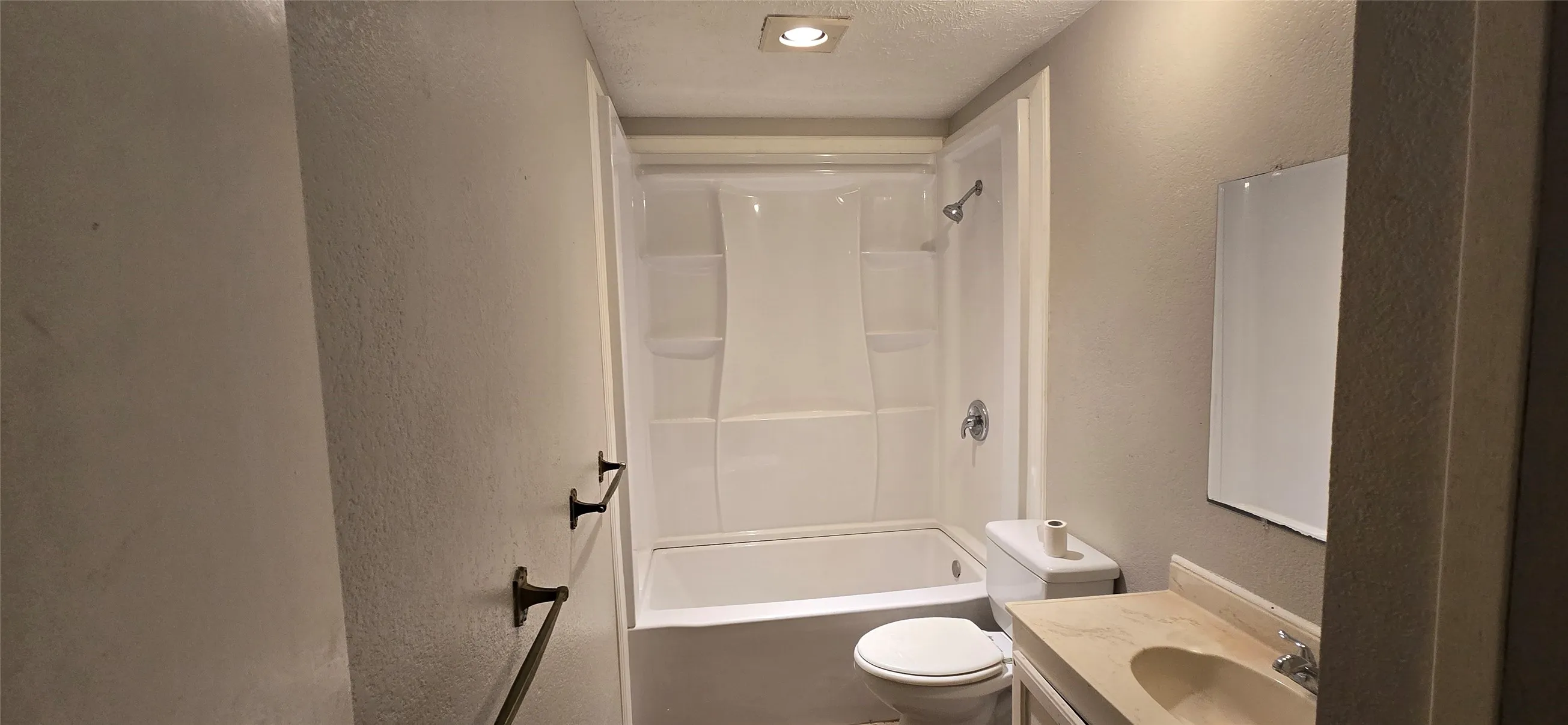 Bathroom featuring a white tub/shower combination with wall-mounted shower head, a toilet, and a vanity with an integrated sink and mirror