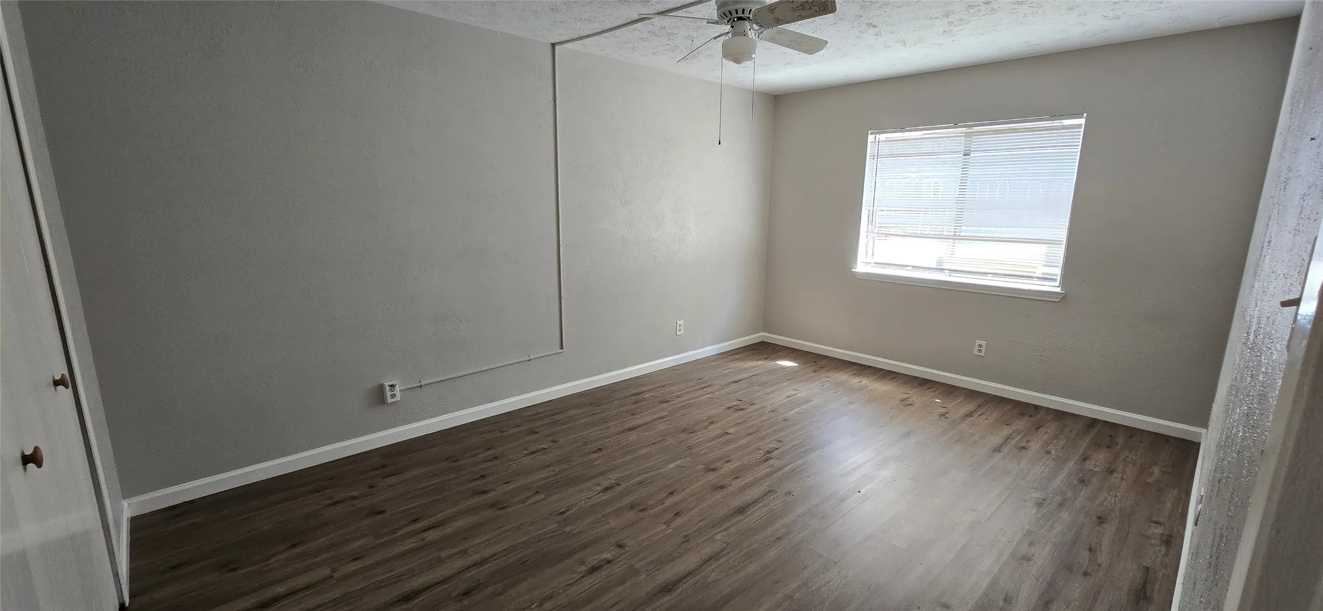 Spacious room featuring wood-finish flooring, light gray walls, a ceiling fan, and a window with blinds
